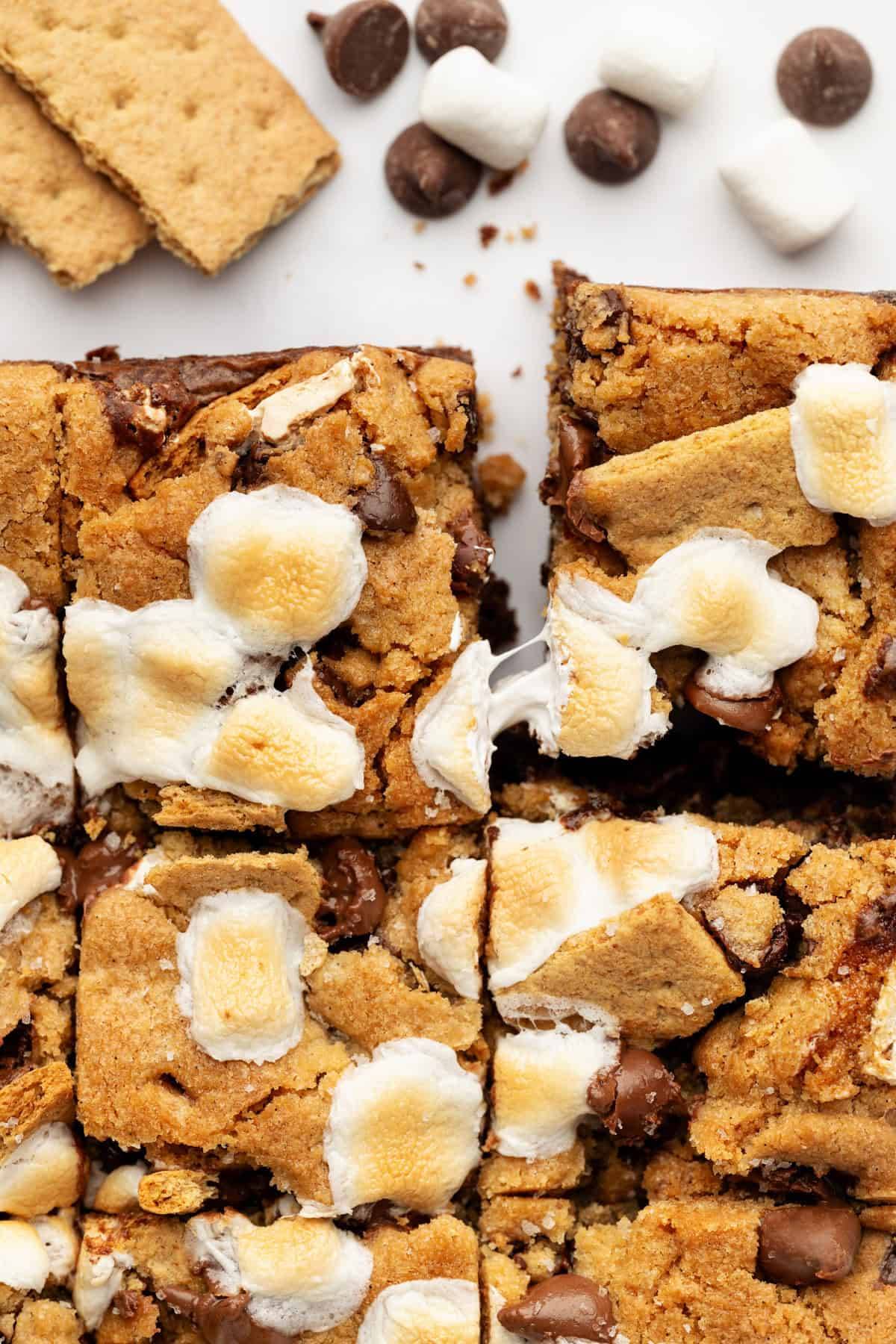 S'mores Bars (a fudgy brownie base, gooey marshmallow creme center, and a soft, golden cookie layer on top. Topped with extra chocolate chips, graham cracker chunks, and toasted mini marshmallows)