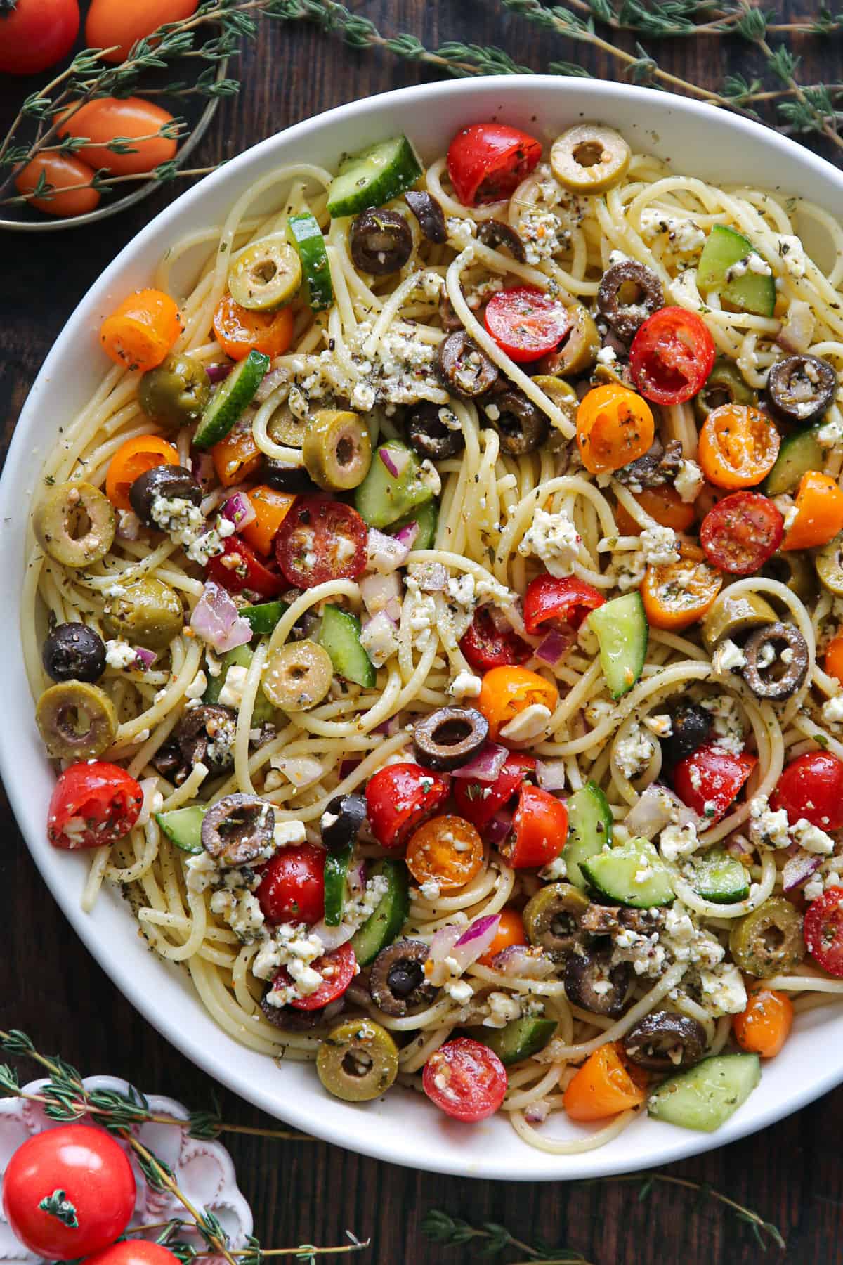Spaghetti Salad features tomatoes, cucumbers, black olives, green olives, red onion, and feta cheese in a large white bowl.