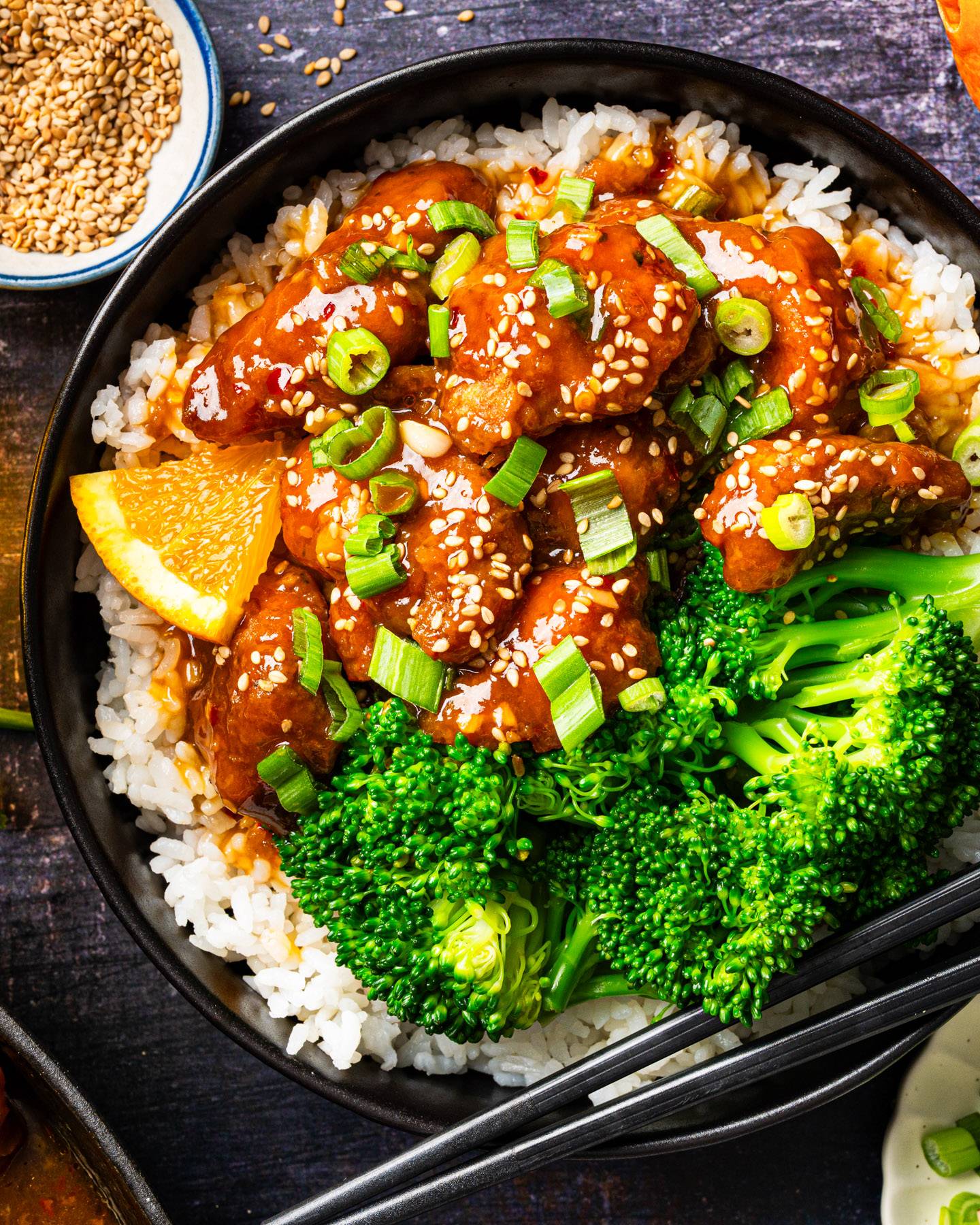 Chinese Orange Chicken with Broccoli and White Rice in a black Bowl.