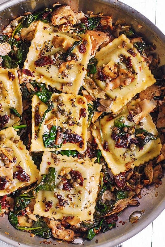 Italian Ravioli with Spinach, Artichokes, Capers, Sun-Dried Tomatoes in a stainless steel pan.