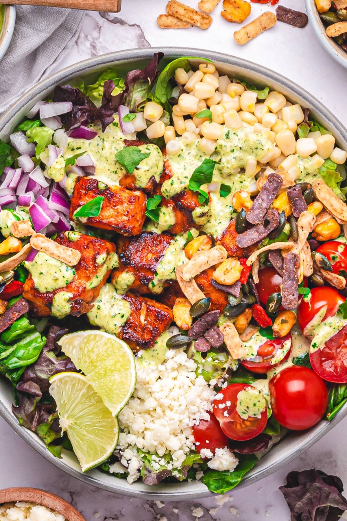 Mexican-Inspired Salmon Taco Salad Bowl with Poblano Ranch Dressing, corn, cherry tomatoes, lettuce, and cotija cheese.