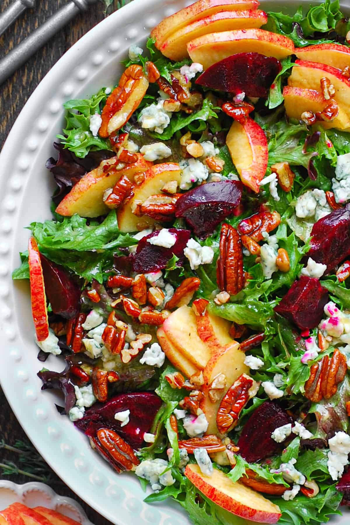 Beet and Apple Salad with Mixed Greens, Pecans, Blue Cheese, and homemade Honey-Lemon Mustard Dressing in a white bowl.