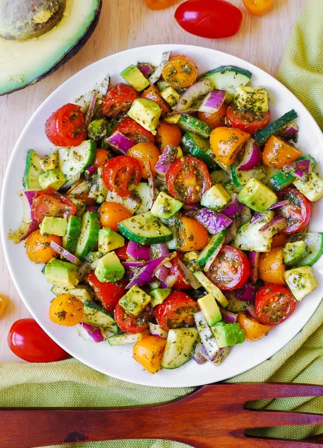 Tomato Cucumber Avocado Salad with Basil Pesto Dressing on a white plate.