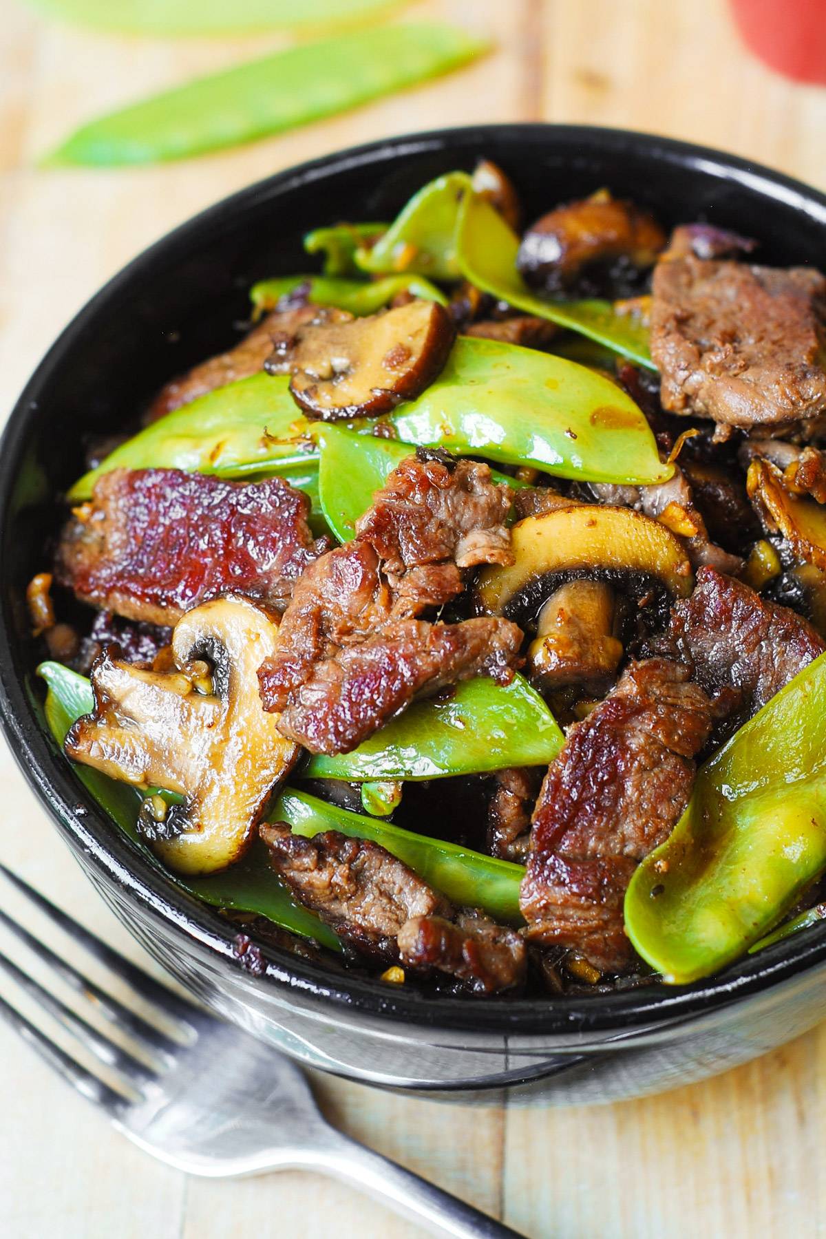 Asian Beef with Mushrooms and Snow Peas in a black bowl.