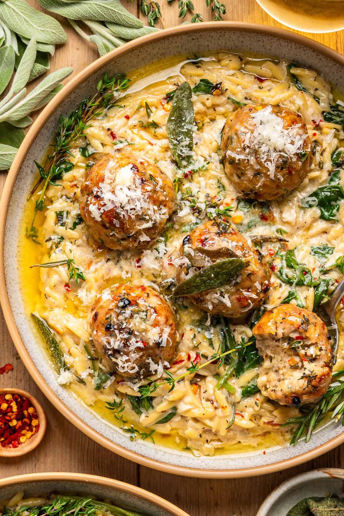 Baked Chicken Meatballs with Creamy Parmesan Spinach Orzo and Garlic-Butter-White-Wine Sauce in a bowl.