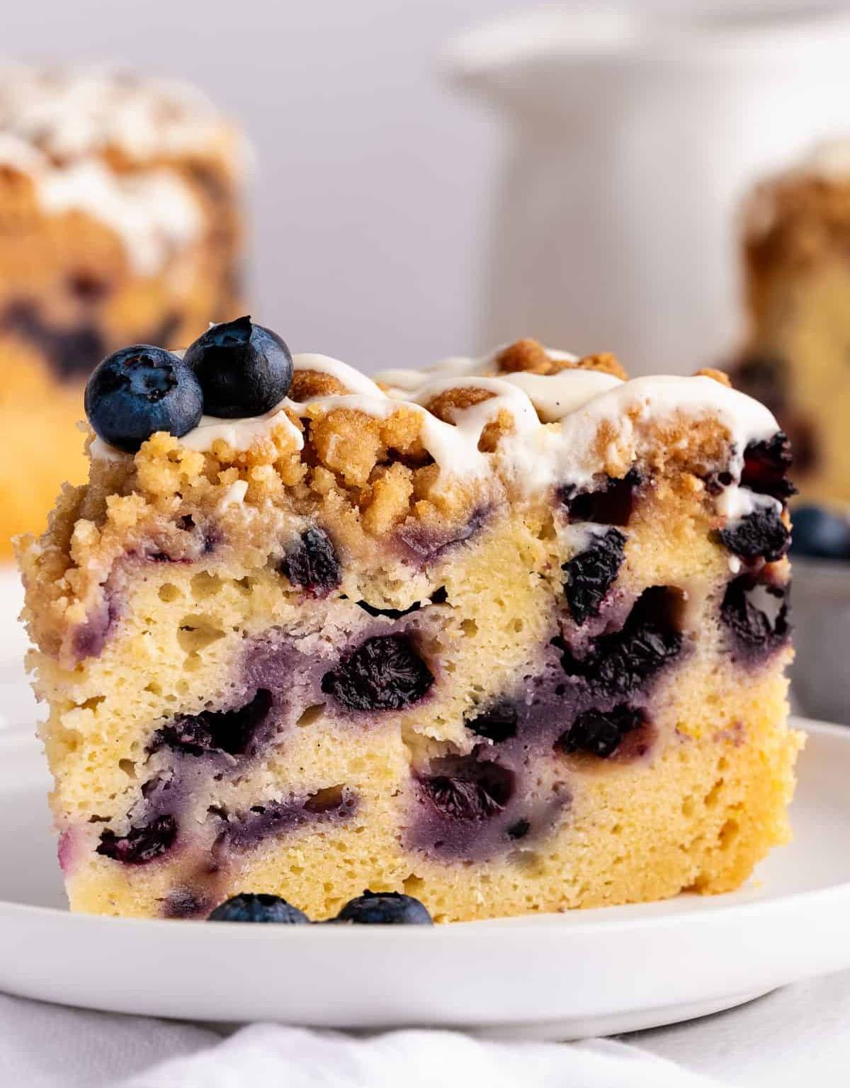A slice of Blueberry Coffee with Streusel Crumble Topping and Lemon Cream Cheese Glaze on a white plate.