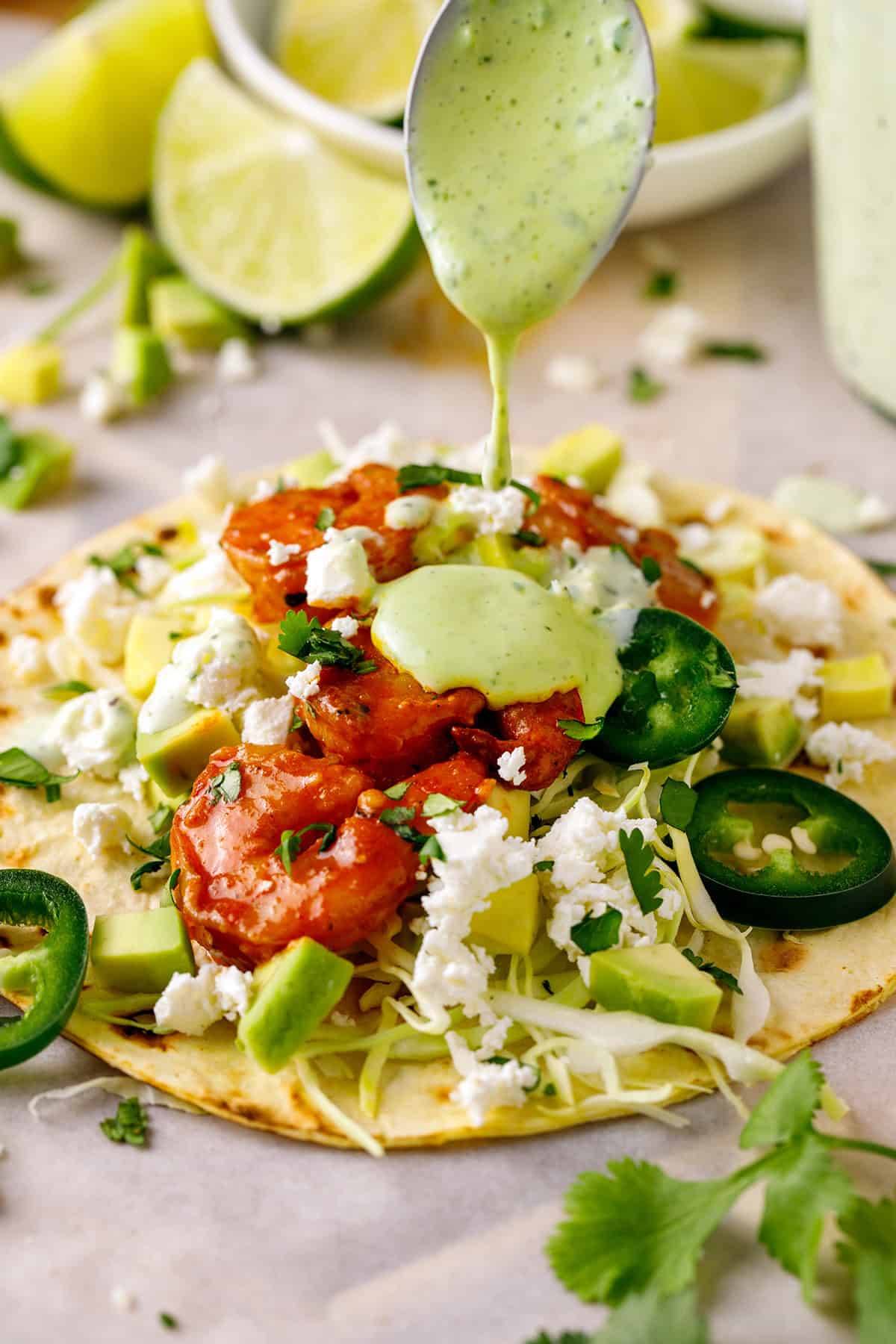 Shrimp Tacos with Cilantro-Lime Crema, Avocado, and Cotija Cheese (or Feta) on a white surface.