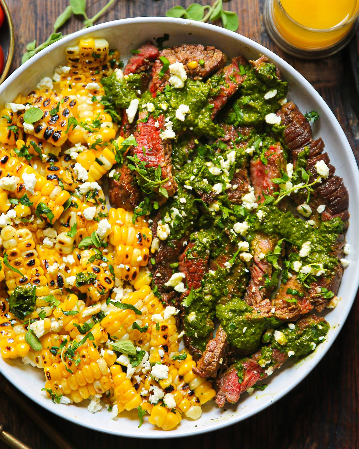 Flank Steak with Grilled Corn, Feta Cheese, and Spinach Pesto on a white plate.