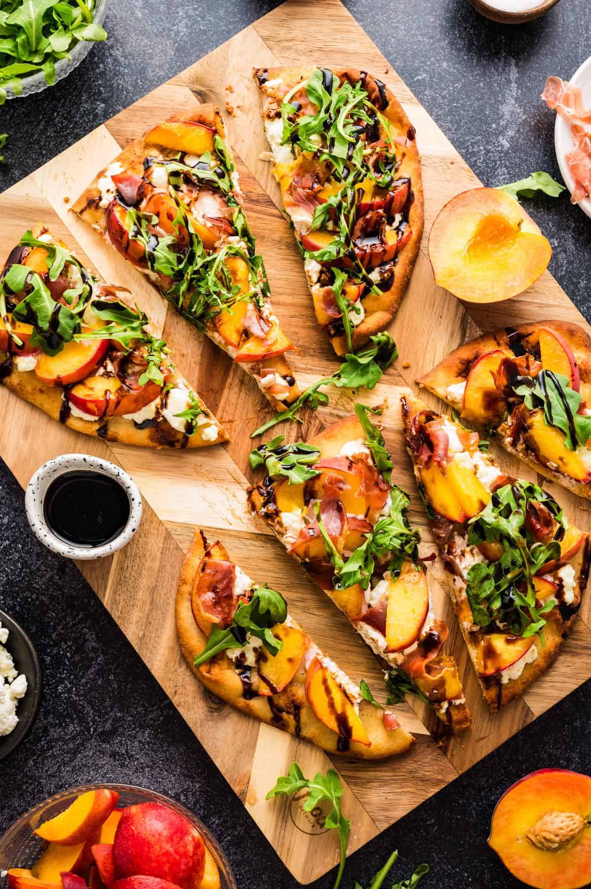 Peach, Goat Cheese, Arugula, & Prosciutto Flatbread with Balsamic Glaze (sliced on a wooden cutting board).