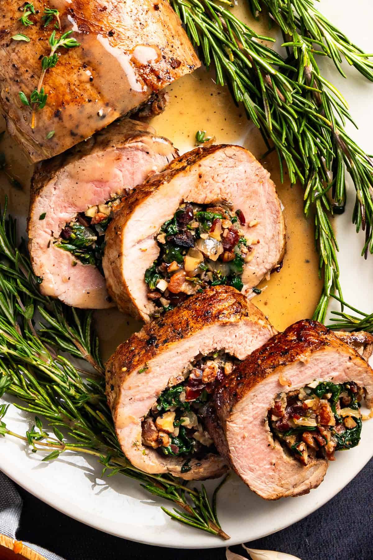 Stuffed Pork Tenderloin (with spinach, cranberries, pecans, and bacon) on a white platter.