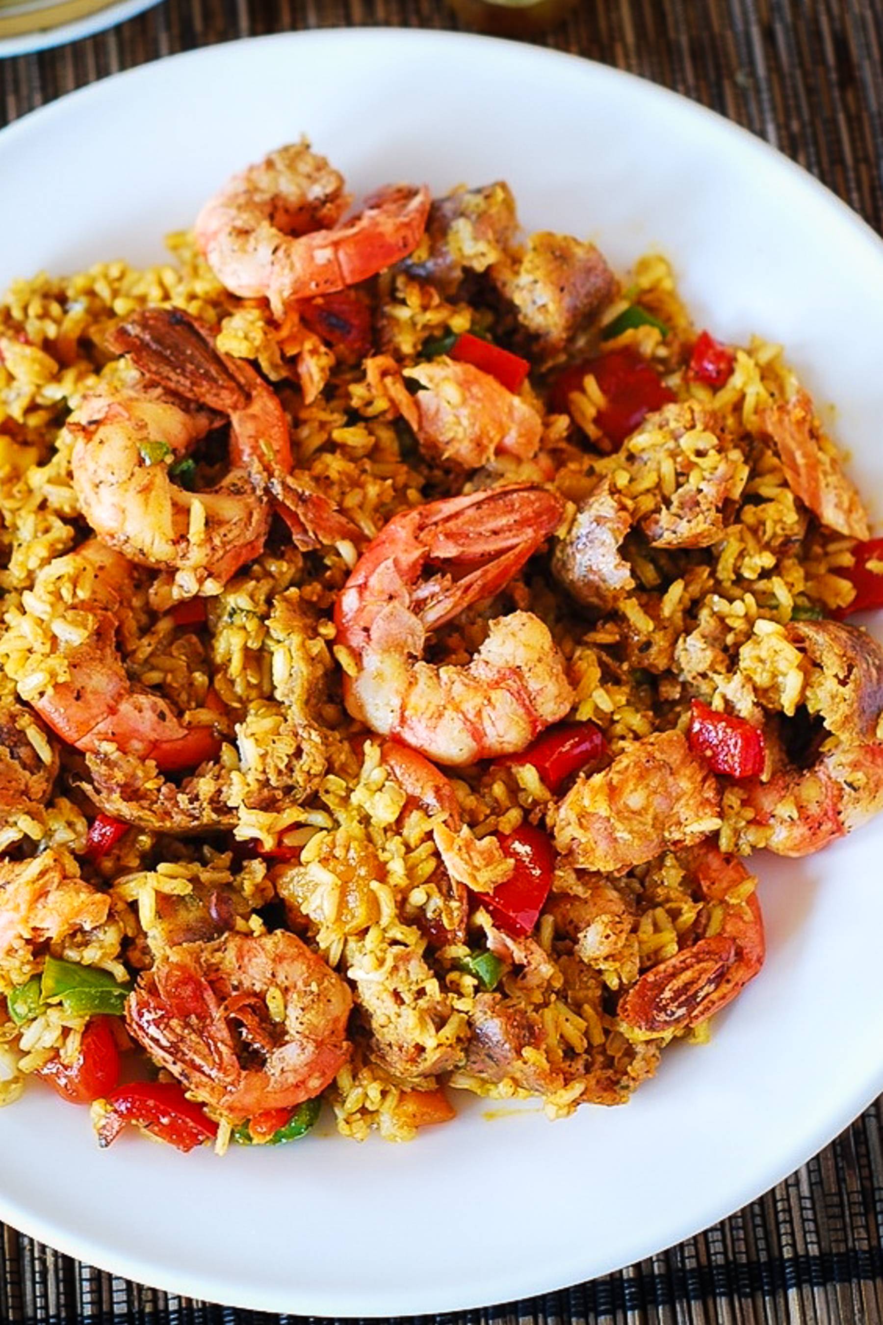 Mixed Paella with Chicken, Shrimp, Sausage, and Bell Peppers on a white plate.