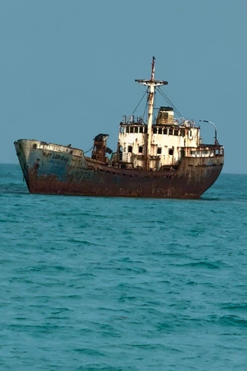 rusty shipwreck sitting in a the shallow ocean waters.