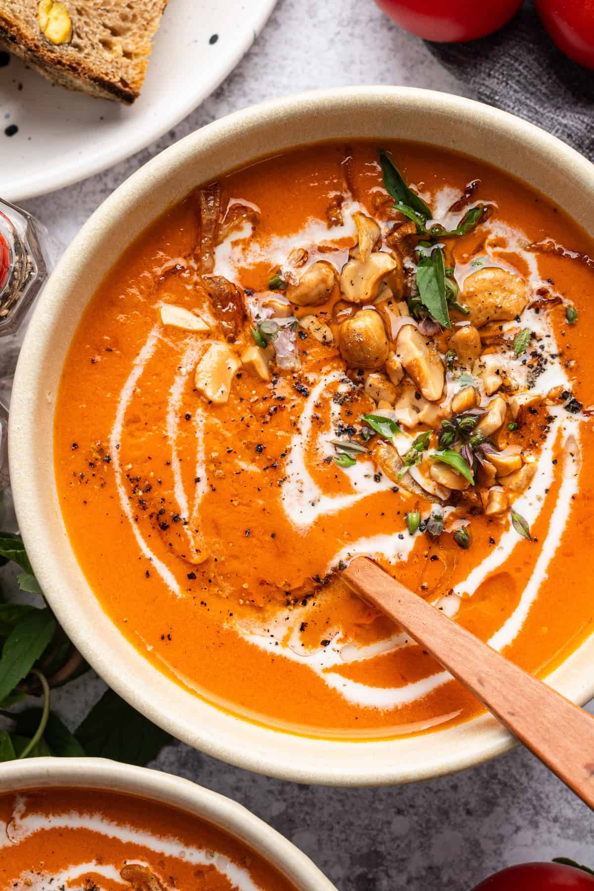 Coconut Tomato Soup with Toasted Cashews, Crispy Shallots, and fresh basil in a white bowl.