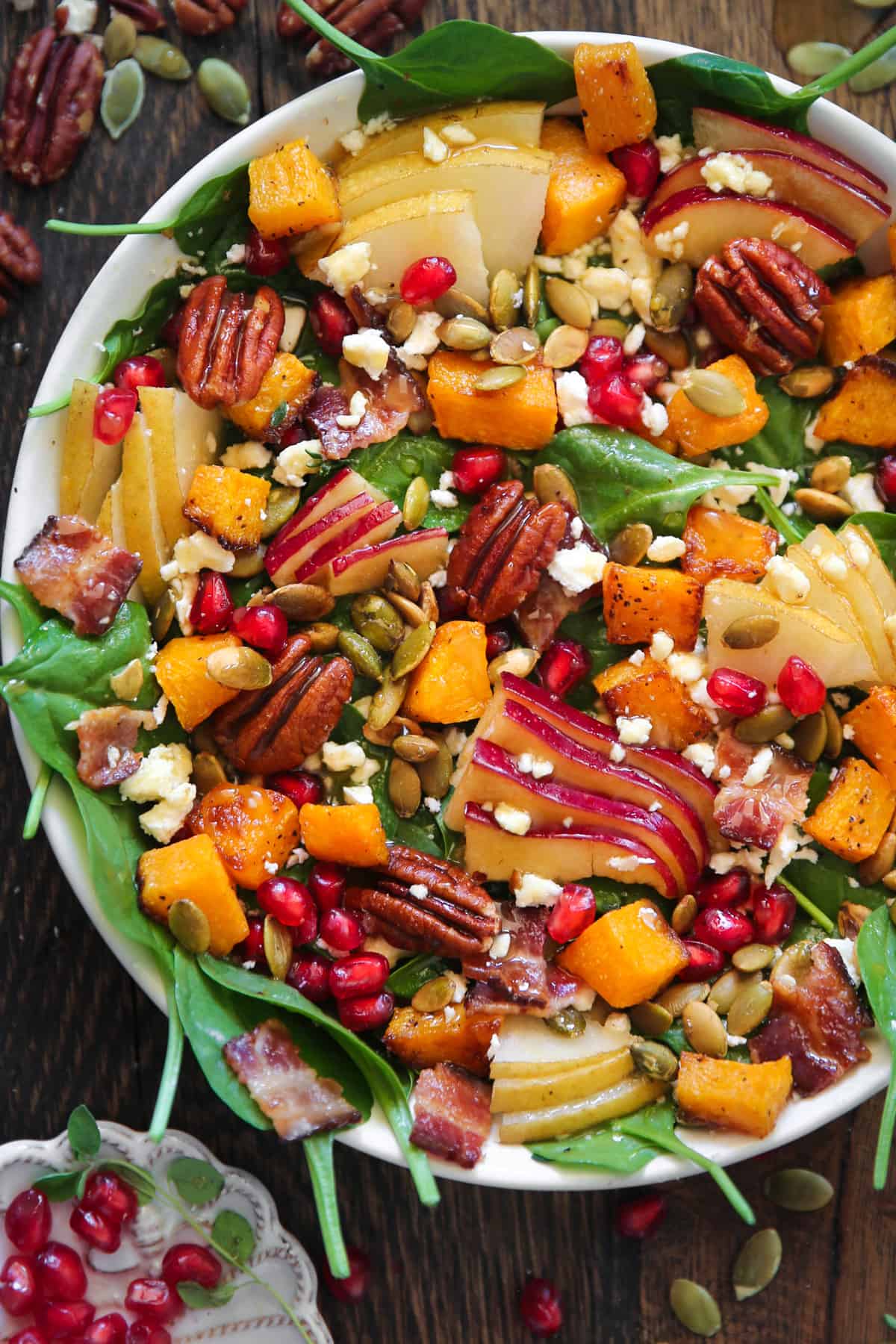 Fall Harvest Salad (with roasted butternut squash, apple, pear, crunchy pecans, pumpkin seeds, pomegranate, spinach, feta cheese) in a bowl.