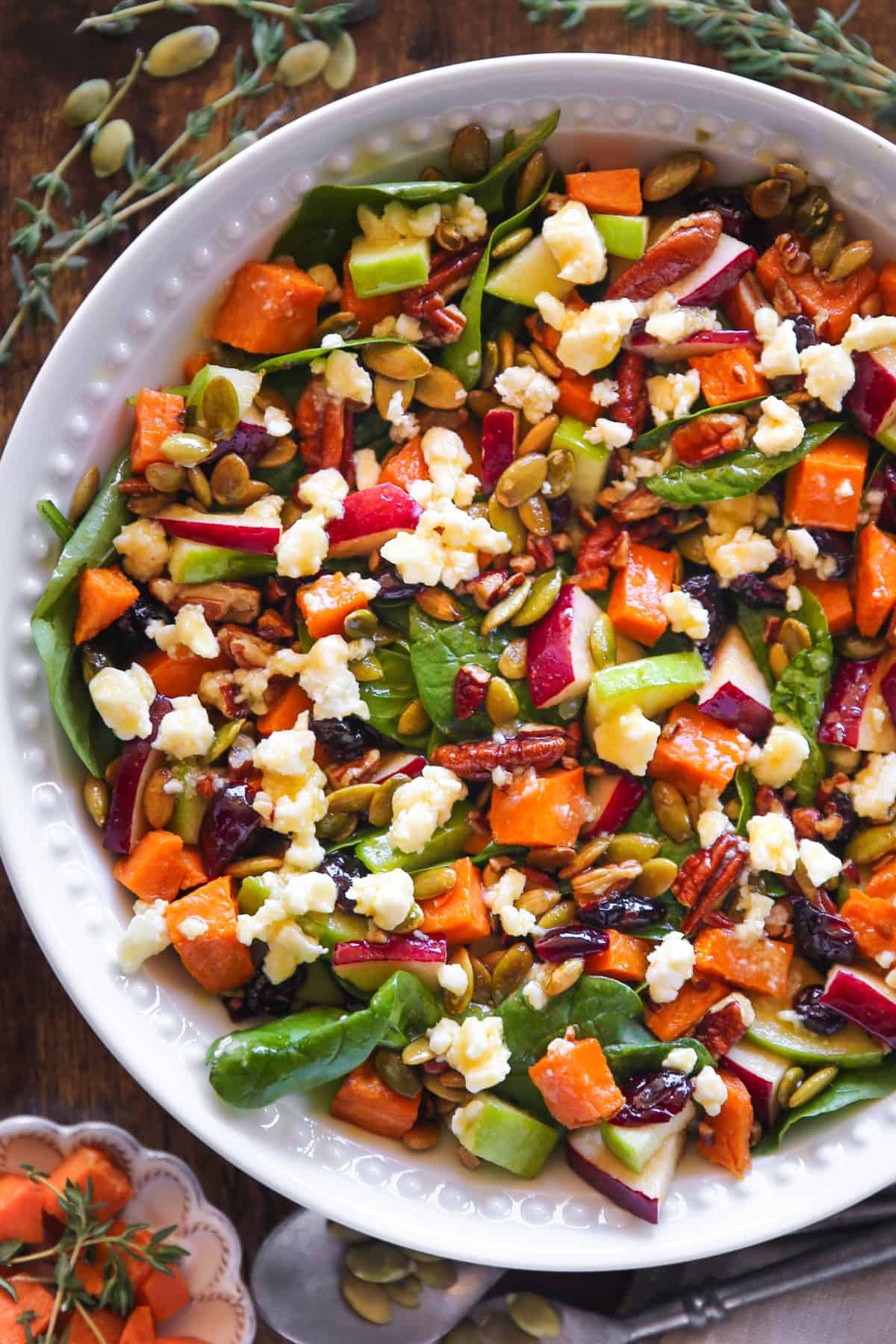 Roasted Sweet Potato Salad features spinach, apples, dried cranberries, pecans, pumpkin seeds, and feta cheese - in a bowl.