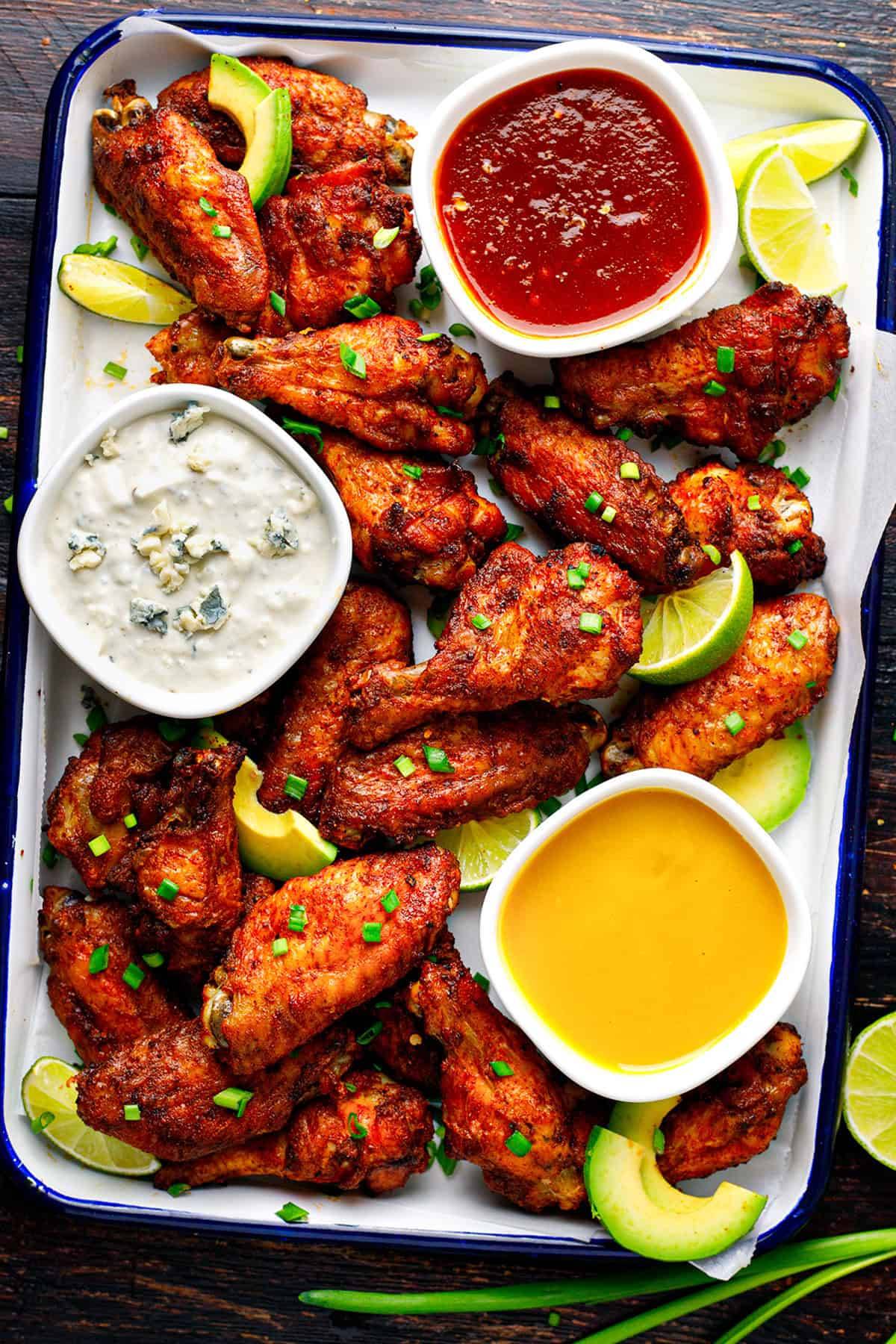 Crispy Baked Chicken Wings​ with 3 Homemade Sauces (Honey Mustard, Blue Cheese, and Honey Sriracha) on a baking sheet.