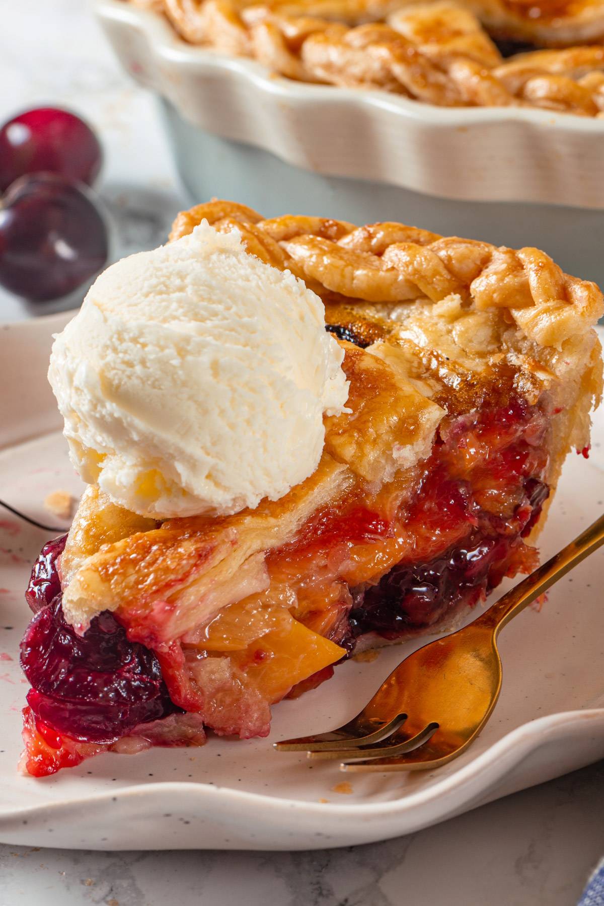 A slice of Peach Cherry Pie with a scoop of ice cream on top of it - on a white plate.