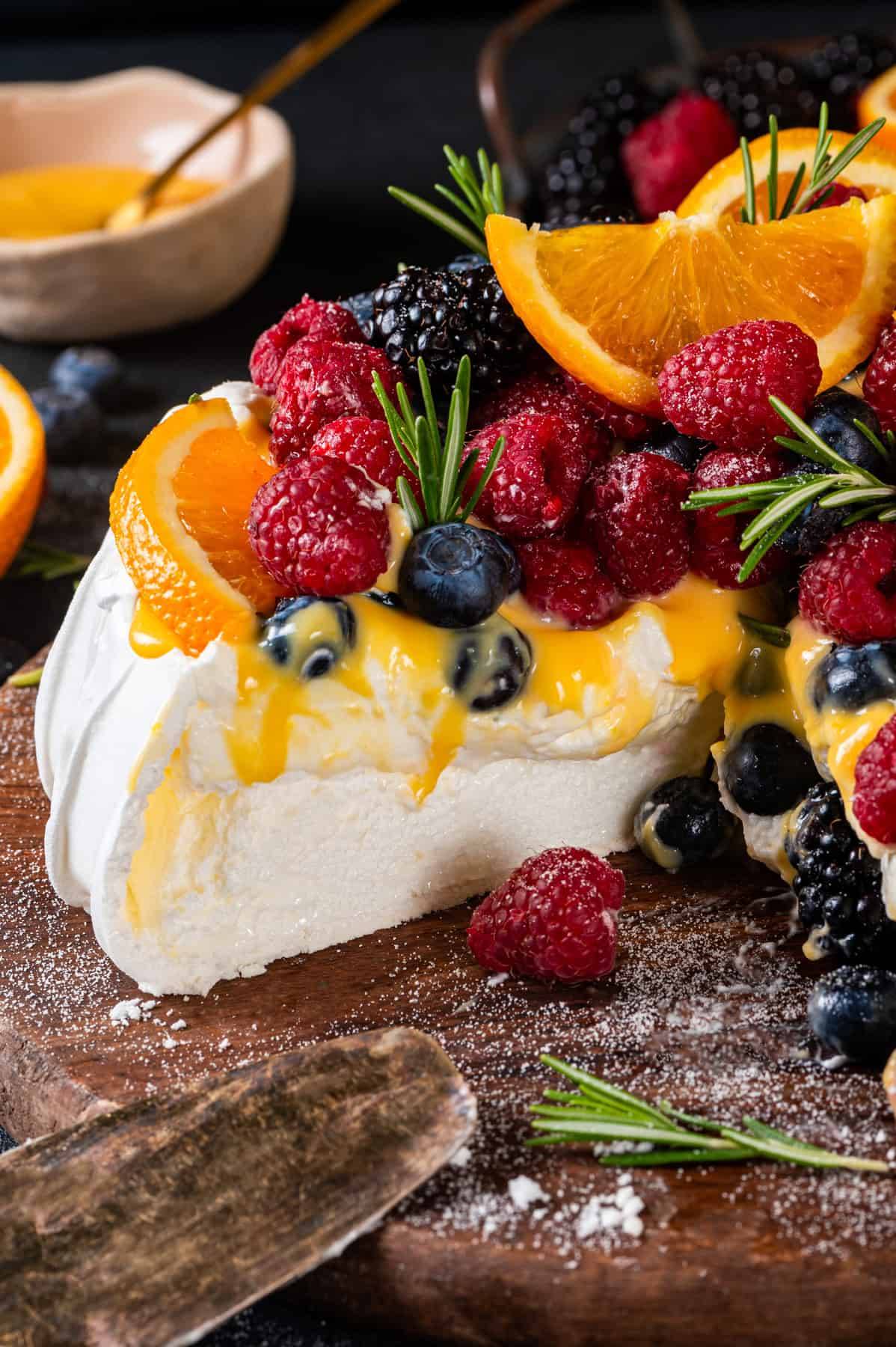 Classic Pavlova (topped with softly whipped cream, orange or lemon curd, fresh berries, and thin orange slices) - on a wooden board.
