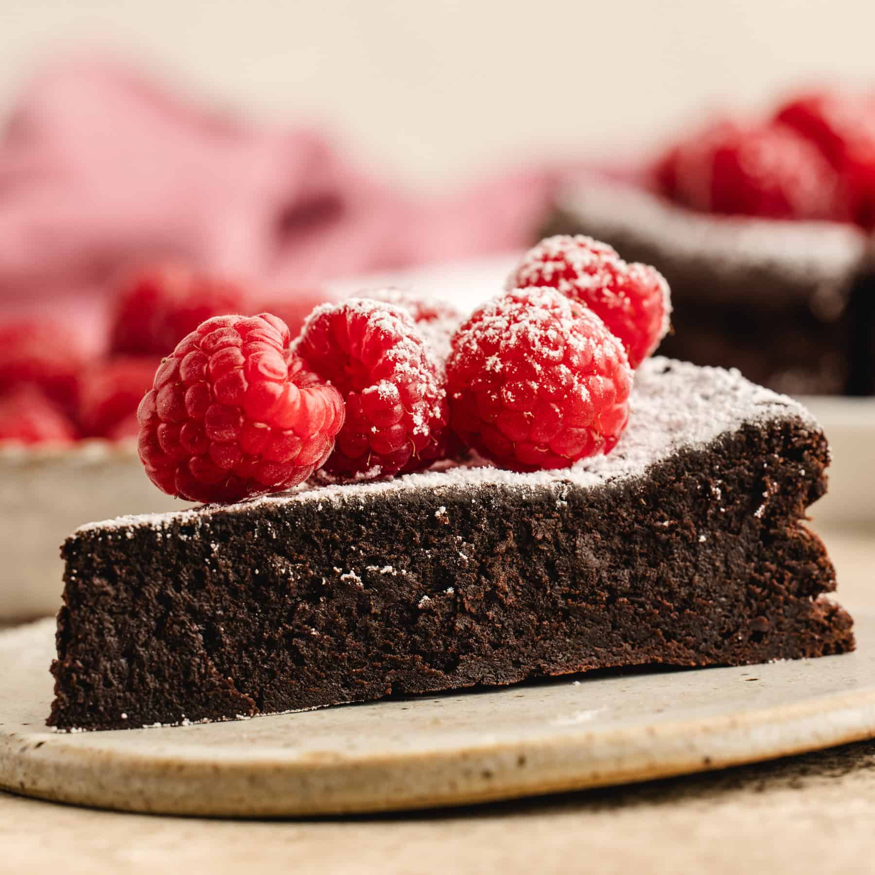 A slice of Flourless Chocolate Cake on a plate (topped with raspberries)