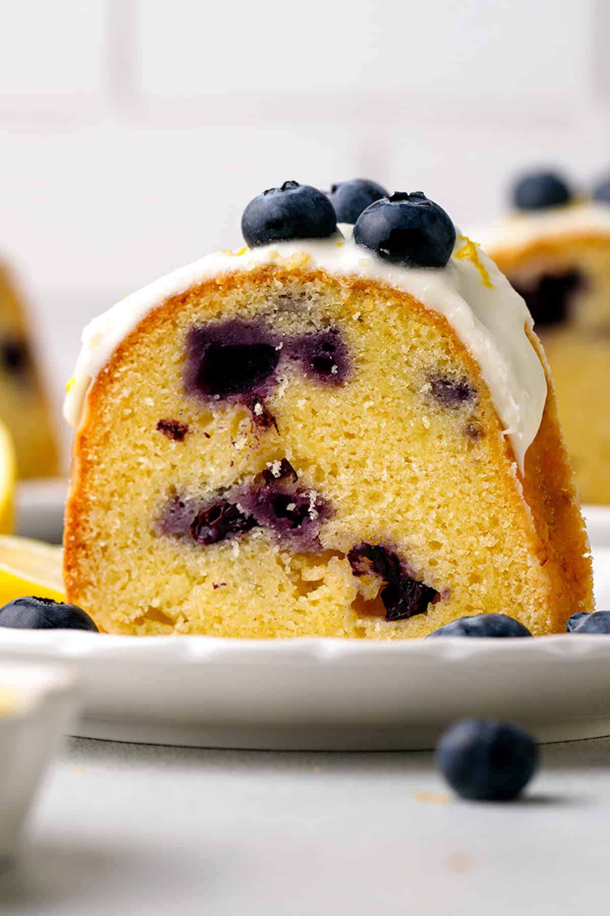 A slice of Lemon Blueberry Bundt Cake with thick lemon glaze - on a white plate.