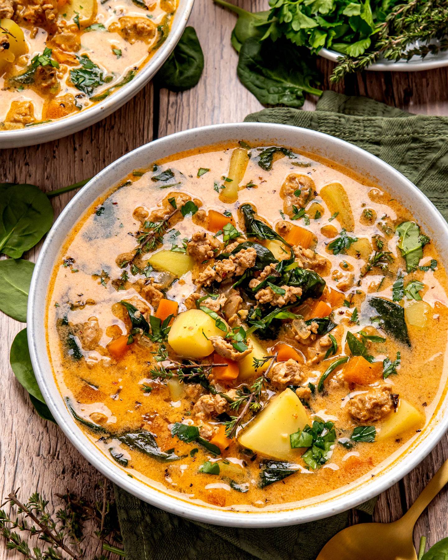 Italian Sausage Potato Soup with Spinach and Carrots in a white bowl.