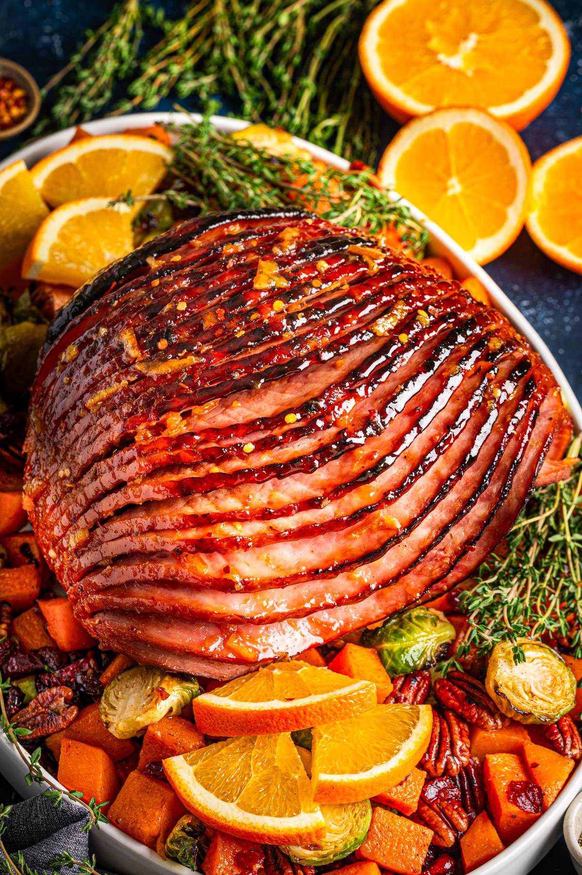 Honey Brown Sugar Glazed Spiral Cut Ham on a platter with roasted Brussels sprouts, butternut squash cubes, pecans, and dried cranberries.