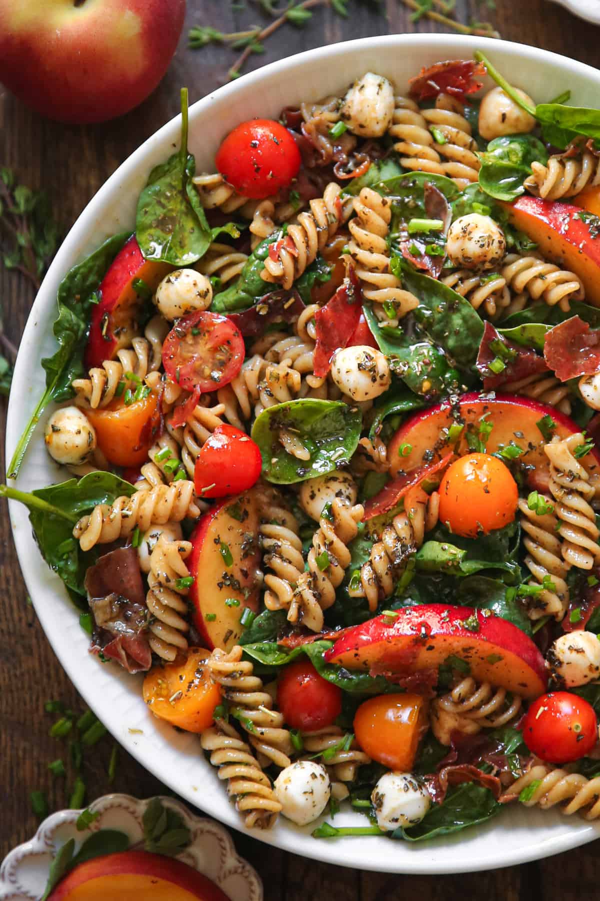 Summer Pasta Salad with Peaches, Spinach, Tomatoes, and Mozzarella Cheese in a white bowl.