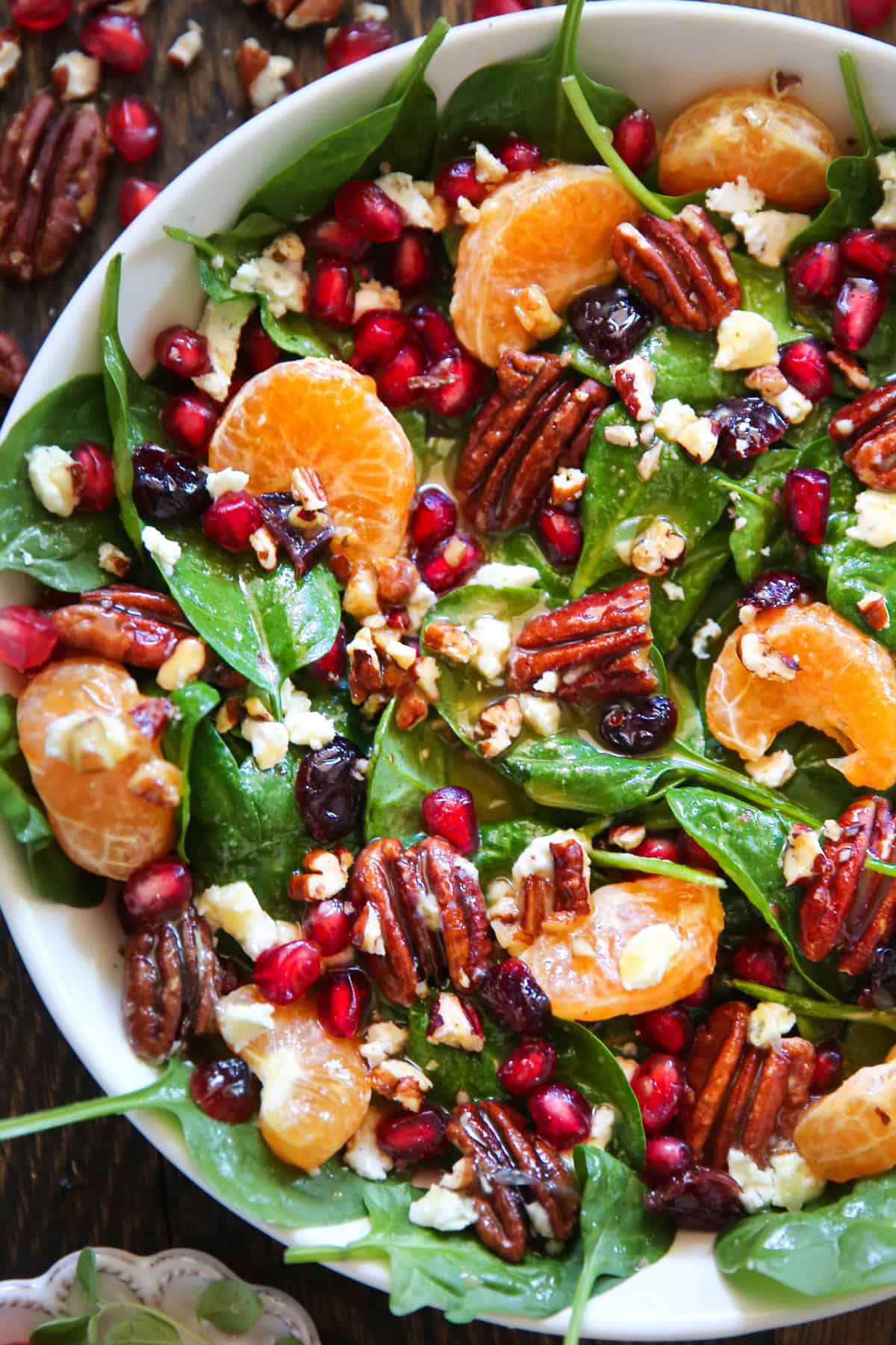 Spinach Salad with Honey-Mustard Lime Vinaigrette (with pecans, mandarin oranges, pomegranate seeds, and dried cranberries) in a white bowl.