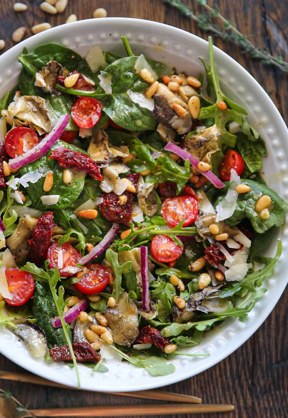 Italian Garden Salad (sun-dried tomatoes, artichokes, cherry tomatoes, pine nuts, Parmesan cheese, and a mix of baby spinach + baby arugula) - in a bowl.