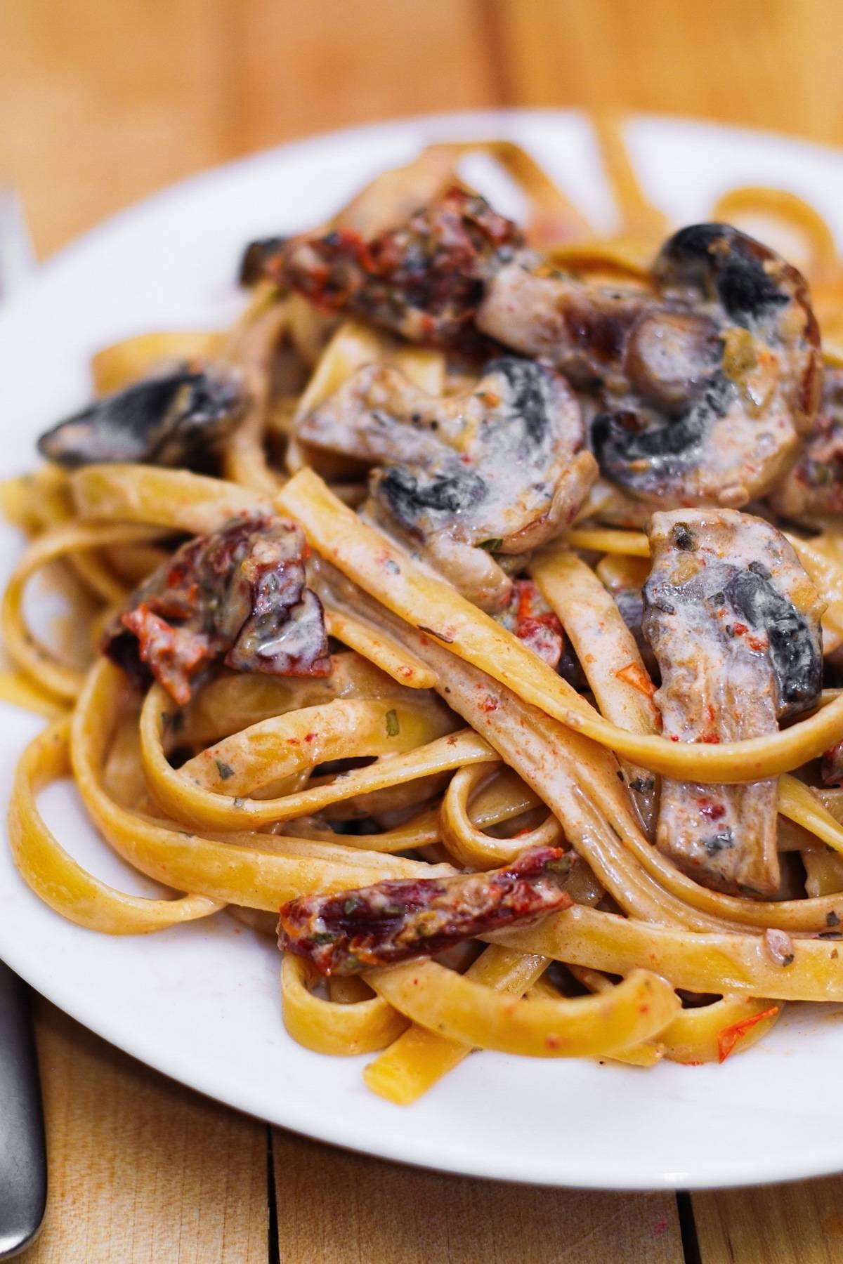 Sun-dried Tomato and Mushroom Pasta in a Garlic and Basil Cream Sauce on a white plate.