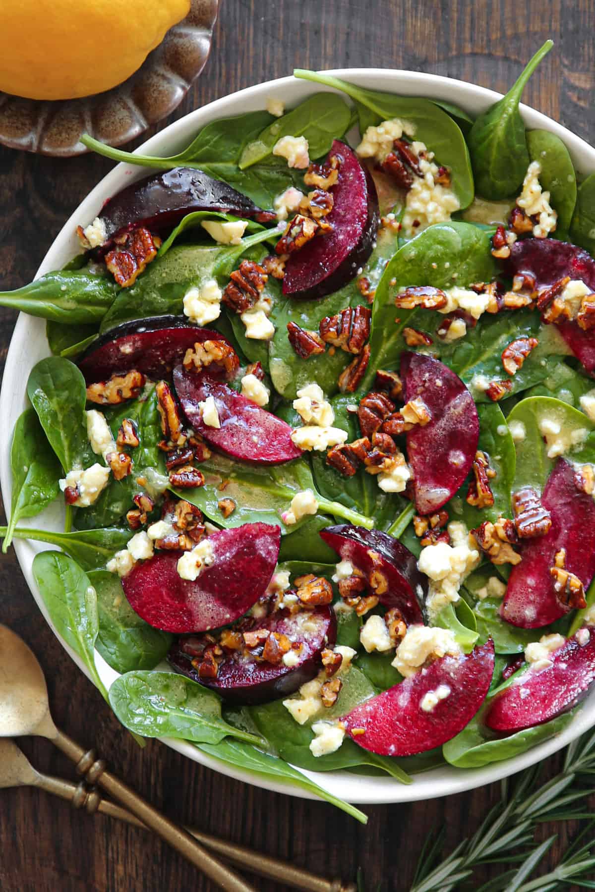 Plum Spinach Salad with Feta Cheese, Pecans, and Honey-Lemon Dressing in a white bowl.