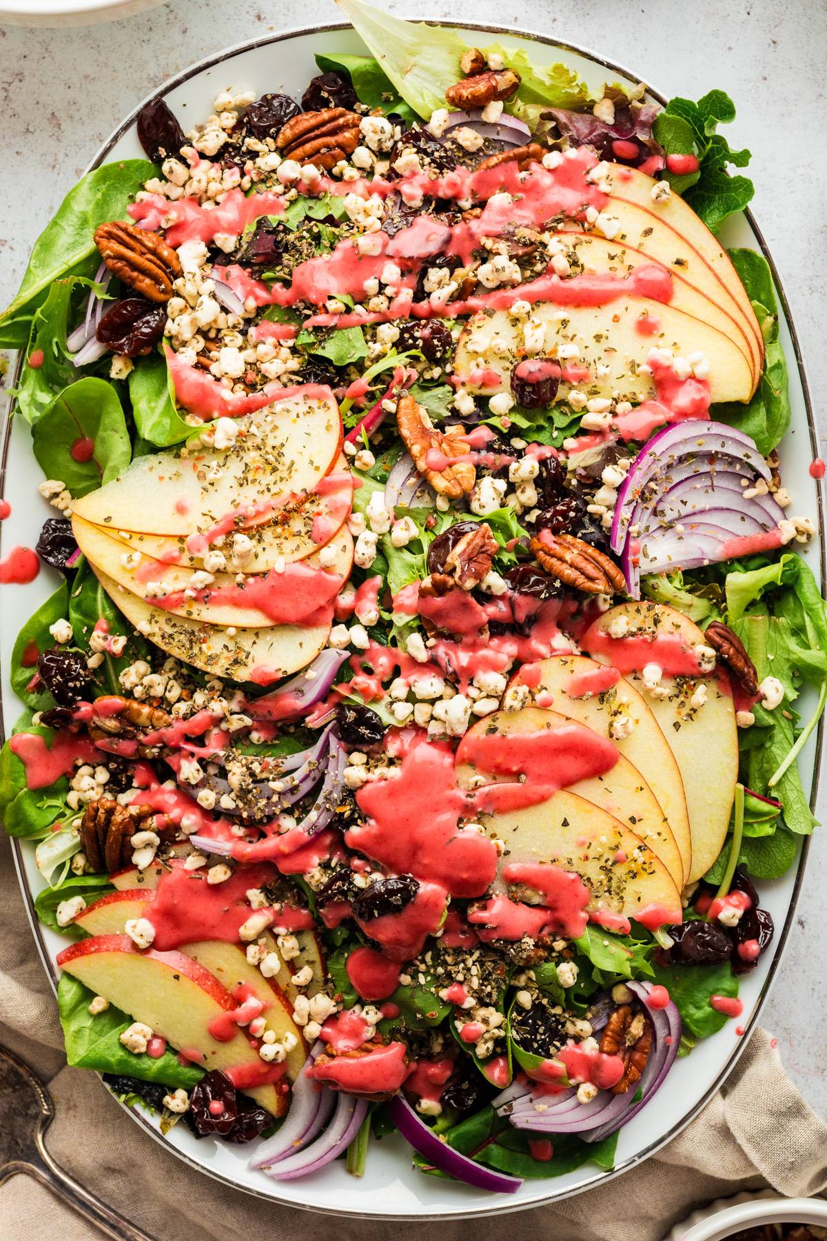 Apple Cherry Green Salad with Raspberry Dressing, Pecans, Goat Cheese, and Red Onion - on a large white platter.