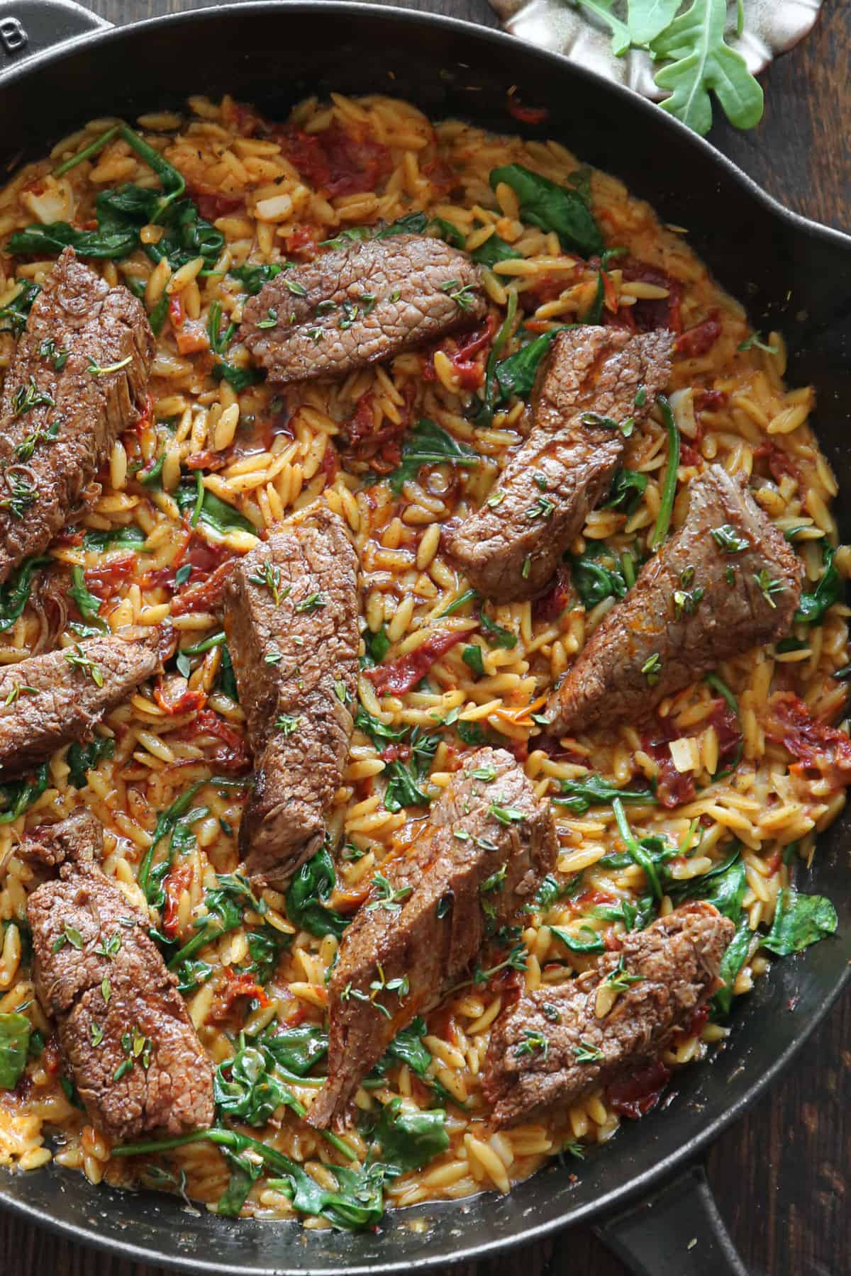 Flank Steak with Creamy Spinach & Sun-Dried Tomato Orzo in a cast iron pan.