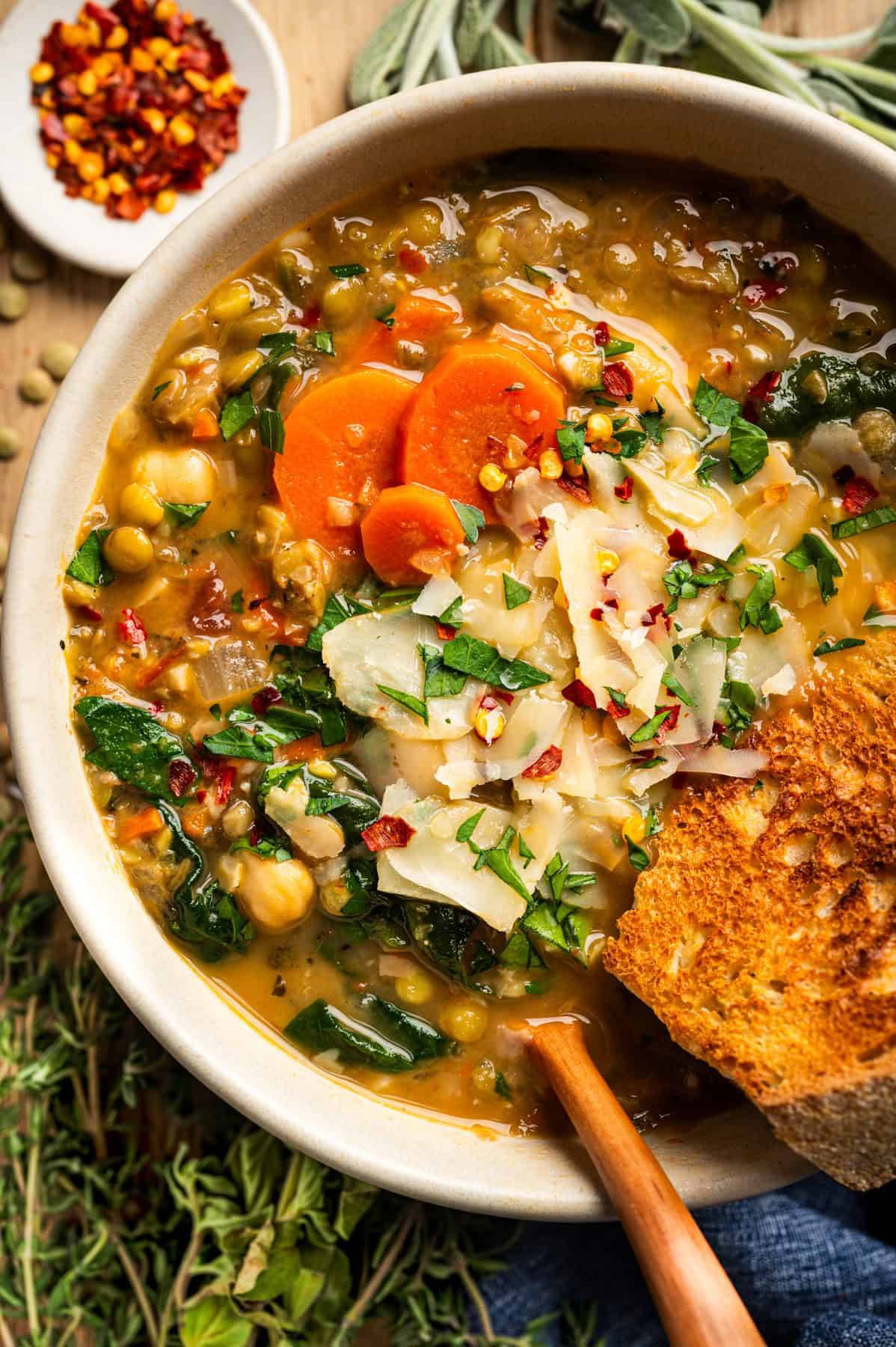 Lentil Soup topped with shaved Parmesan cheese and a crusted slice of bread - in a bowl.