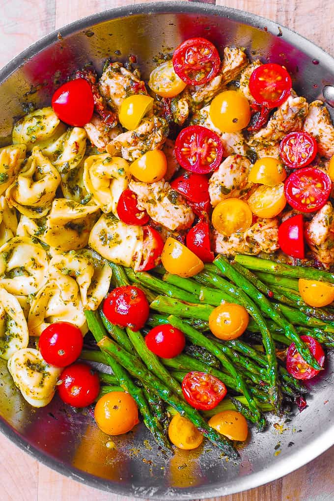 Pesto Chicken Tortellini and Veggies (Cherry Tomatoes and Asparagus) in a stainless steel pan.