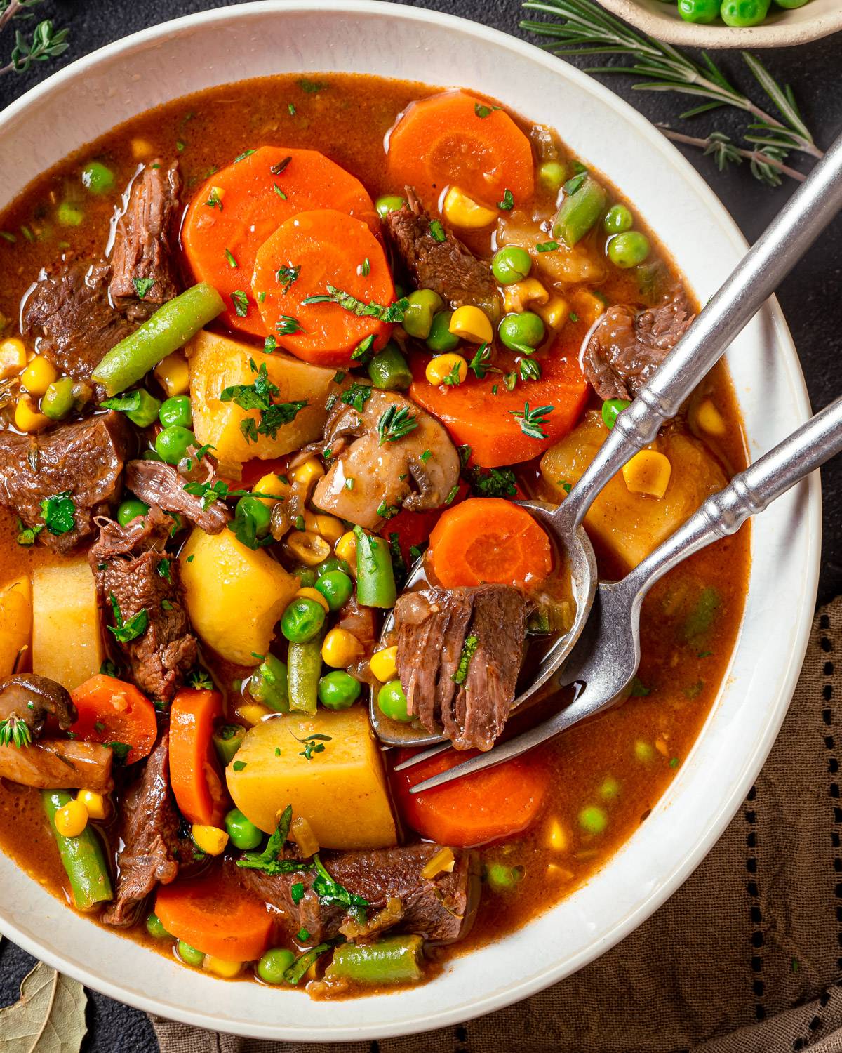 Mulligan Stew with stew beef, potatoes, carrots, corn, peas, and a rich, savory beef broth - in a white bowl.
