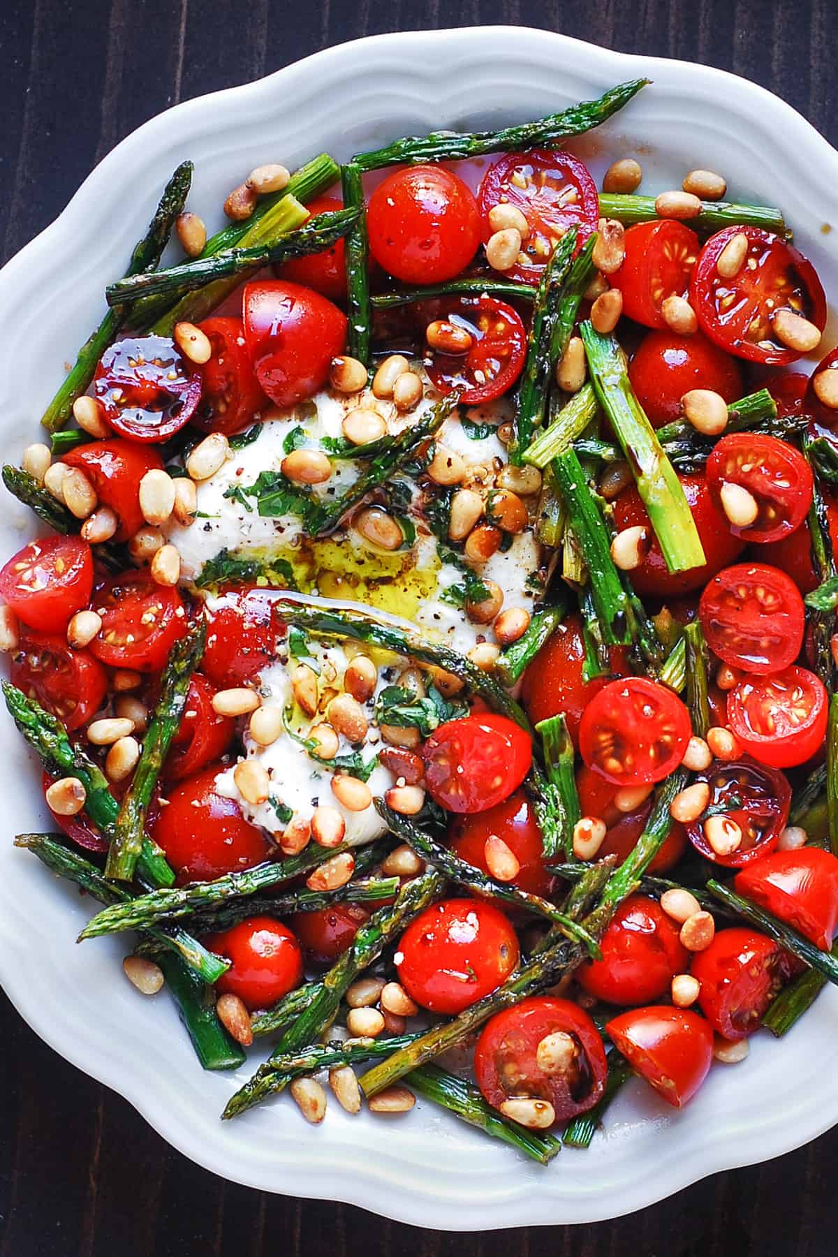Asparagus Tomato Salad with Burrata Cheese and Pine Nuts on a white plate.
