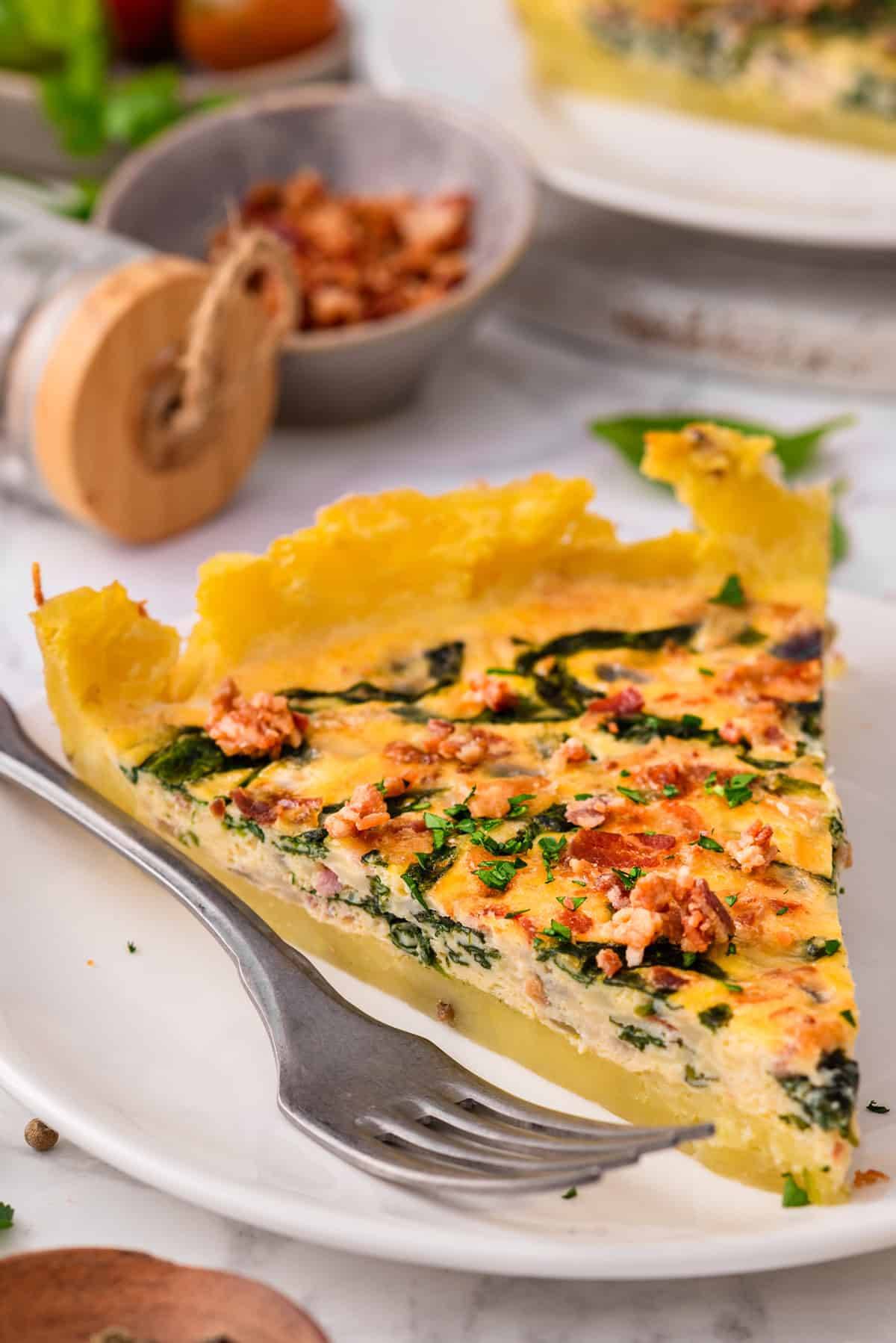 A slice of Gluten-Free Potato Crust Quiche (with spinach, bacon, and cheddar) on a plate.
