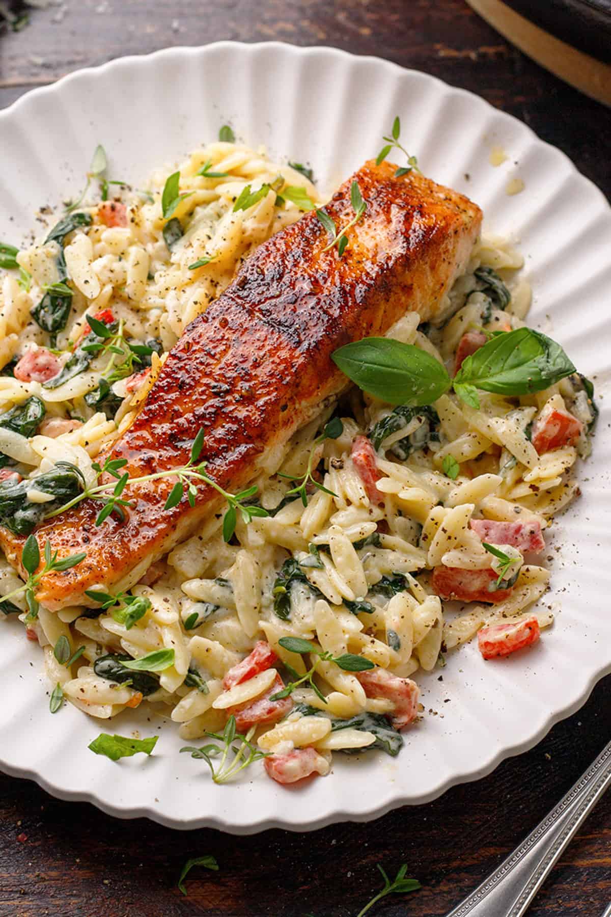 Creamy Salmon Orzo (with spinach, roasted red bell peppers, Parmesan, and a splash of lemon juice) on a white plate.