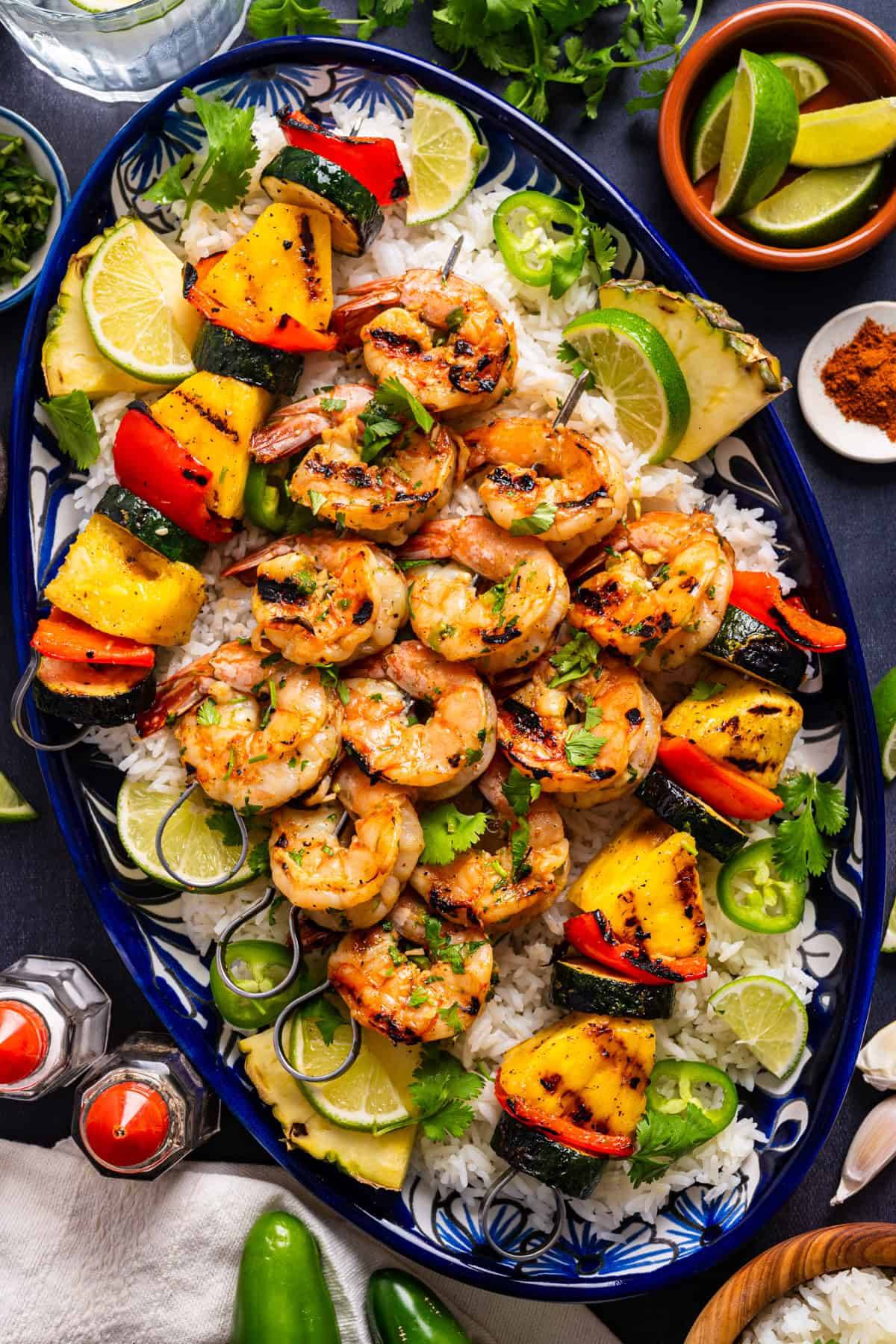 Tequila-Lime Shrimp Skewers with Veggie-Pineapple Skewers over white rice on a blue plate.