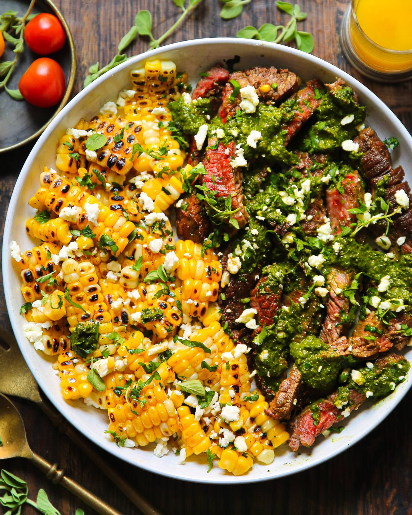 Flank Steak with Grilled Corn, Feta Cheese, and Spinach Chimichurri Sauce on a white plate.