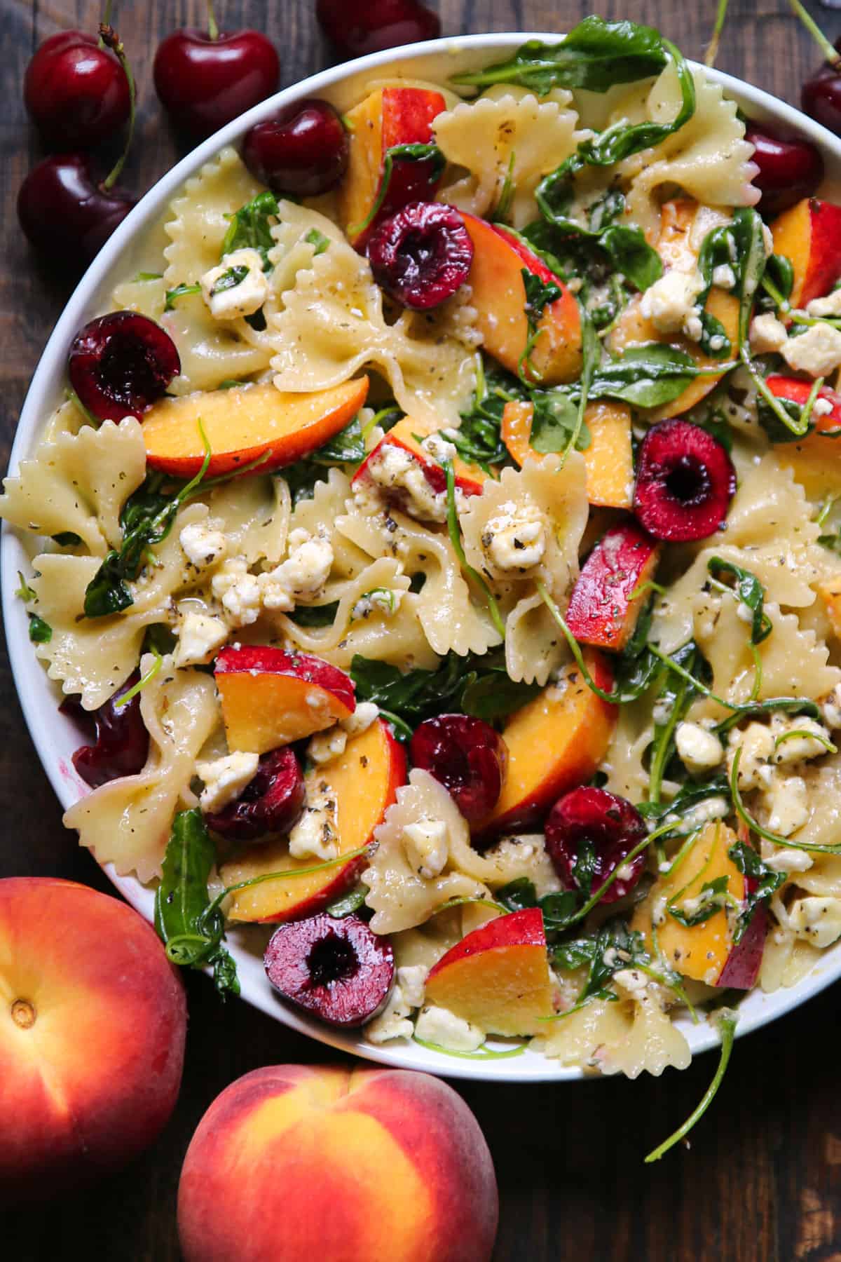 Summer Stone Fruit Pasta Salad with fresh cherries, peaches, feta cheese, and arugula in a white bowl.