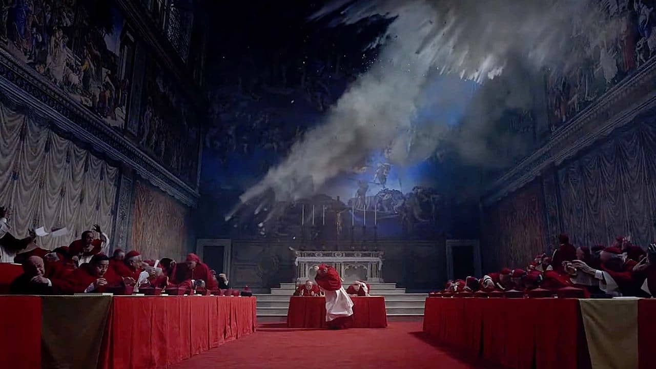 A wide shot of a large chapel where seated priests duck for cover from an explosion outside the windows.