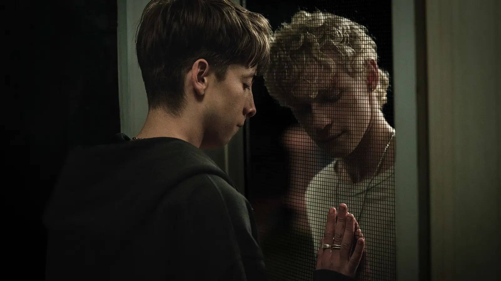 Naim (Joe Bird) and Ryan (Stacy Clausen) reach toward each other through a wire screen door in Leviticus (2026).