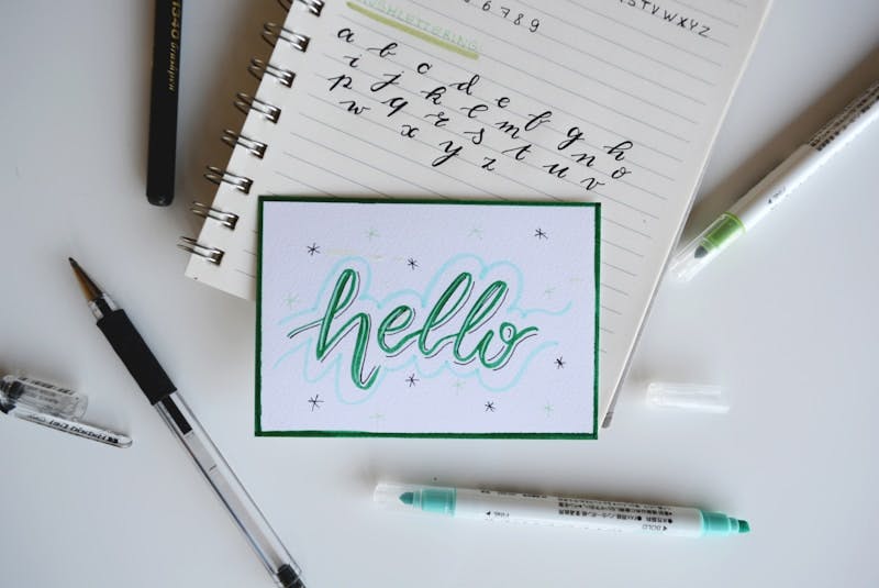 A piece of paper with "Hello" written in cursive with fancy markers.
