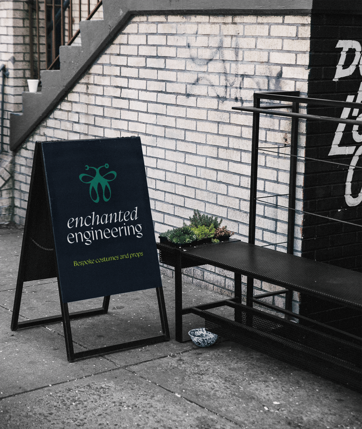 A frame sign with Enchanted Engineering branding. A butterly logo mark, with nuts and bolts for the antannae.