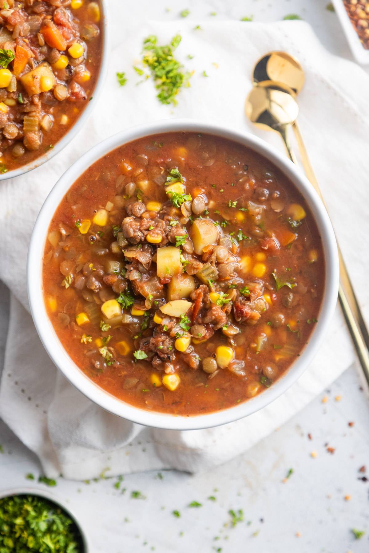 Lentil vegetable soup in a bowl with spoons on the side.