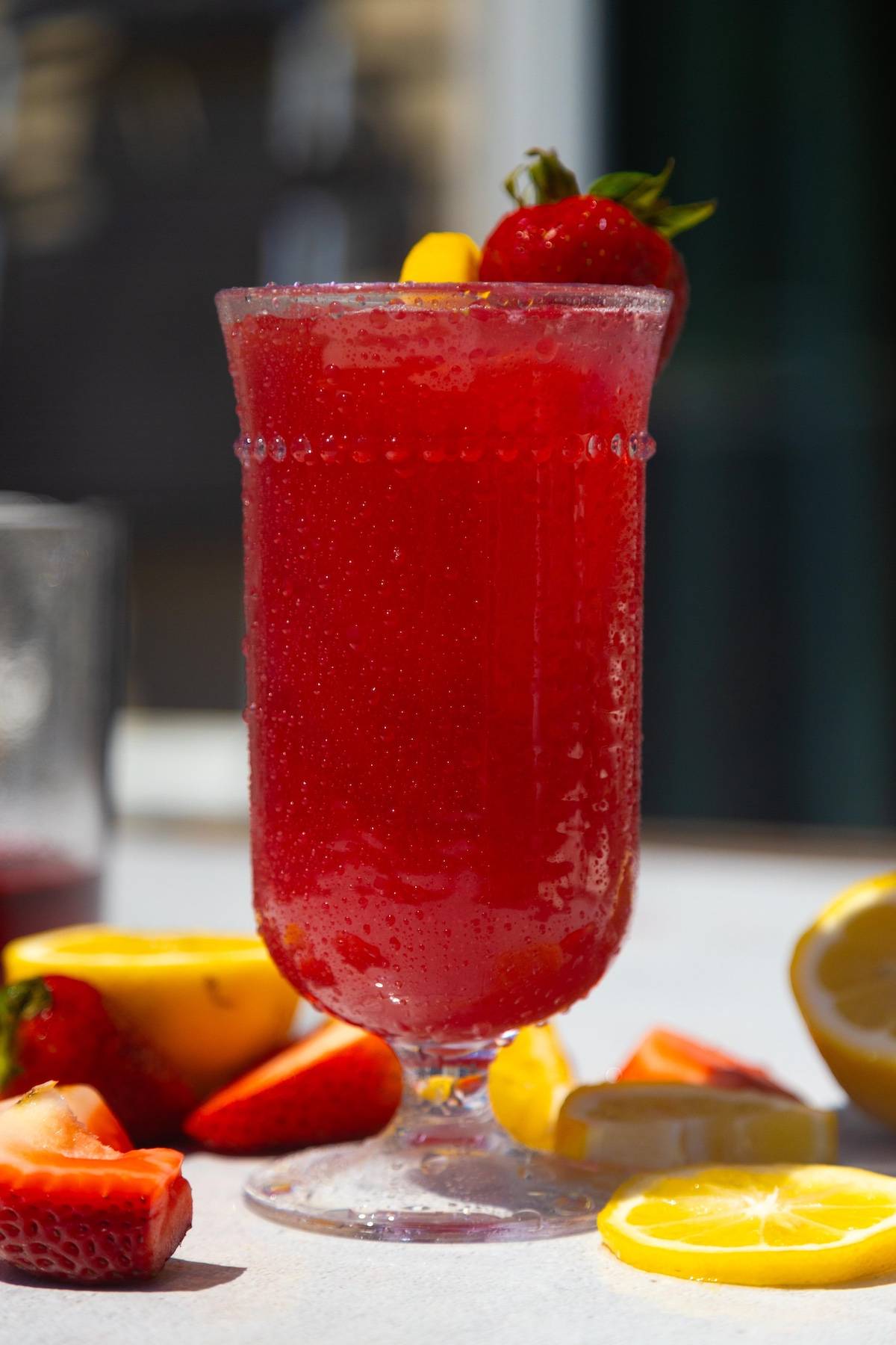 A hibiscus strawberry lemonade drink with a lime wedge on the side.