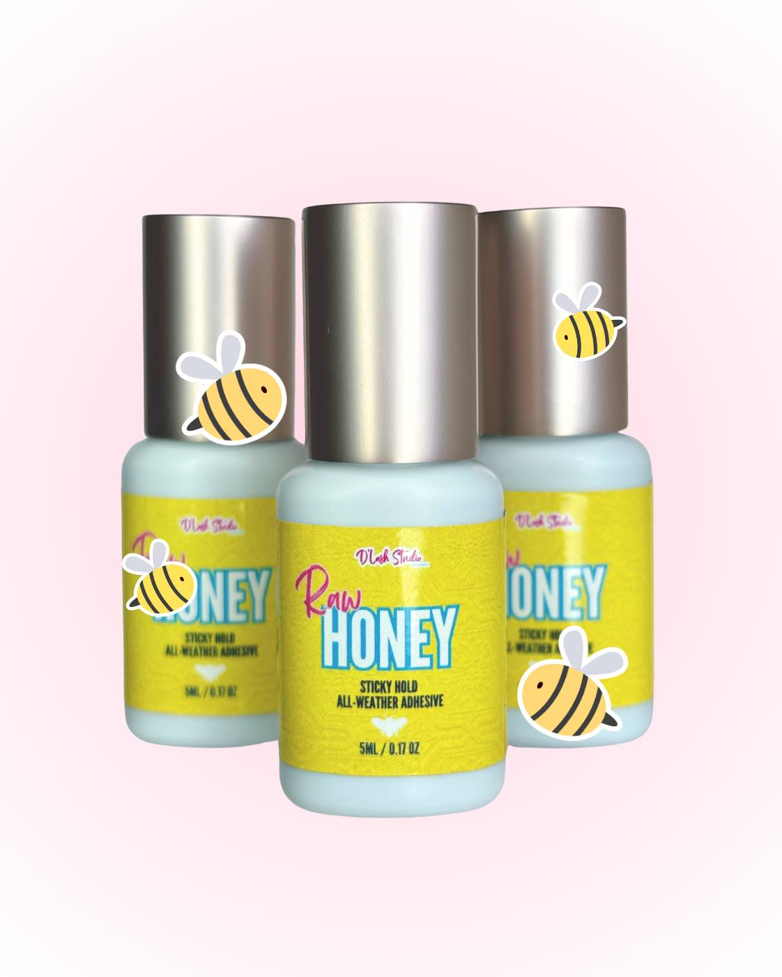 Three bottles of Raw Honey all-weather lash adhesive with bee stickers on a pink background