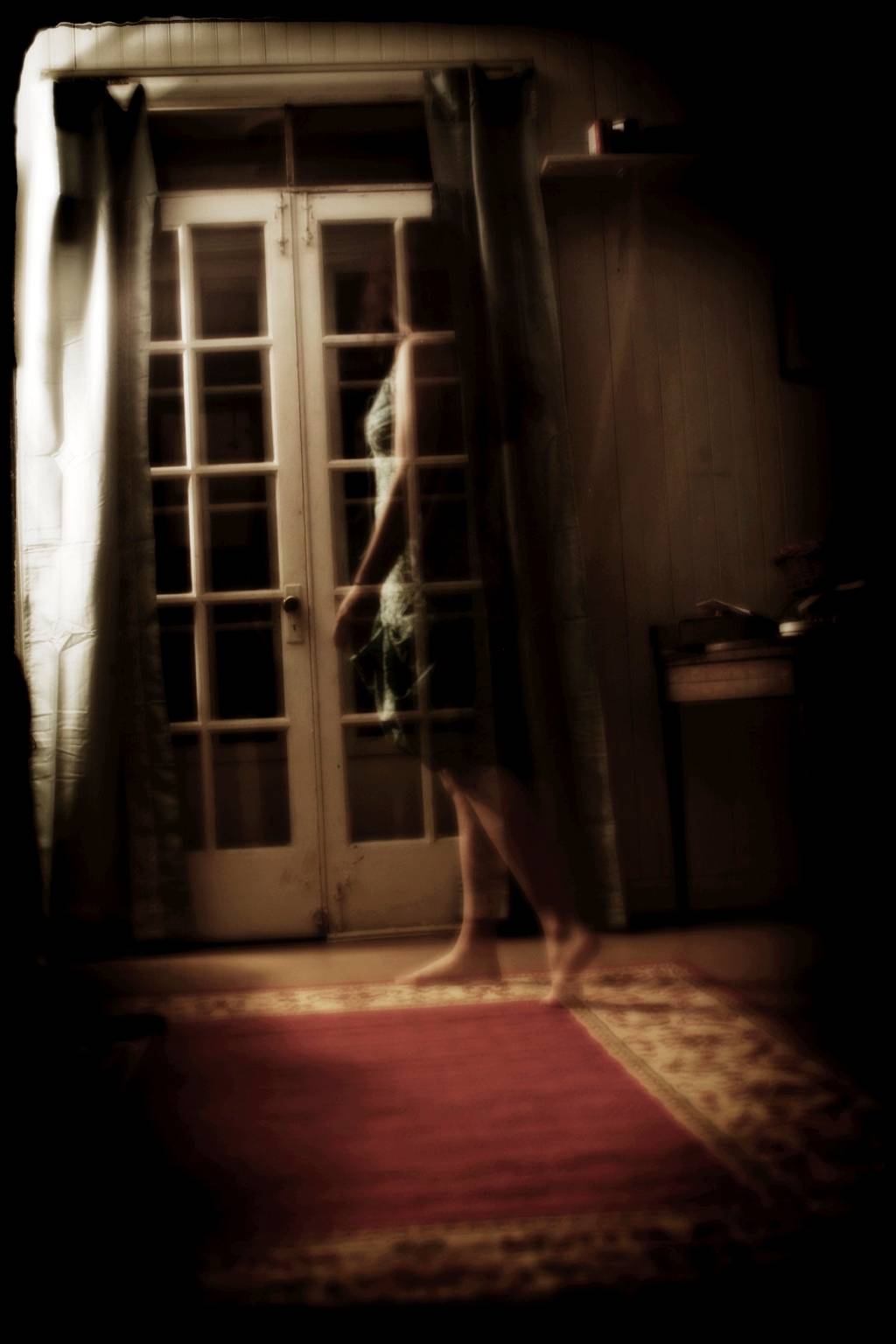 A haunting, ghostly photograph of a translucent woman approaching french doors in the dark of night.